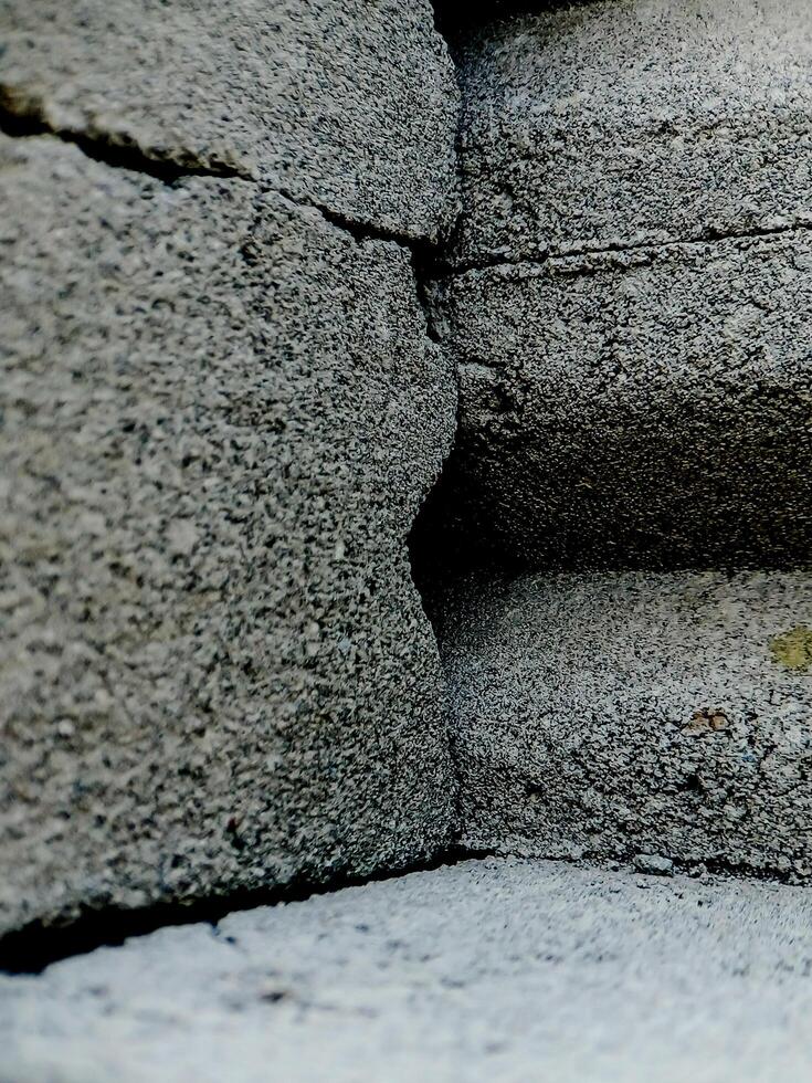 weathered concrete surface, showcasing the rough texture, cracks, and shadows created by its uneven surface. photo