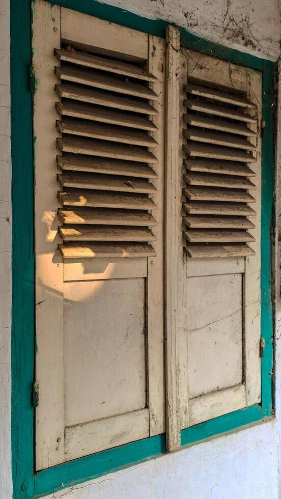 A pair of old, wooden window shutters painted in light beige with a teal frame. photo
