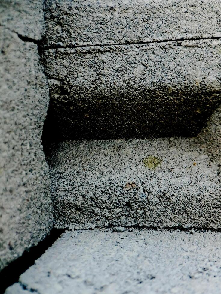 weathered concrete surface, showcasing the rough texture, cracks, and shadows created by its uneven surface. photo
