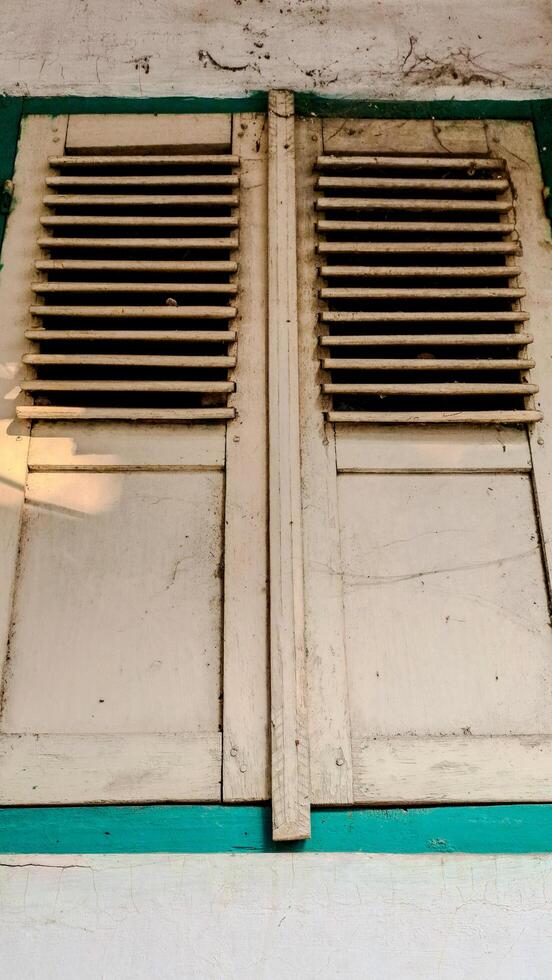 A pair of old, wooden window shutters painted in light beige with a teal frame. photo