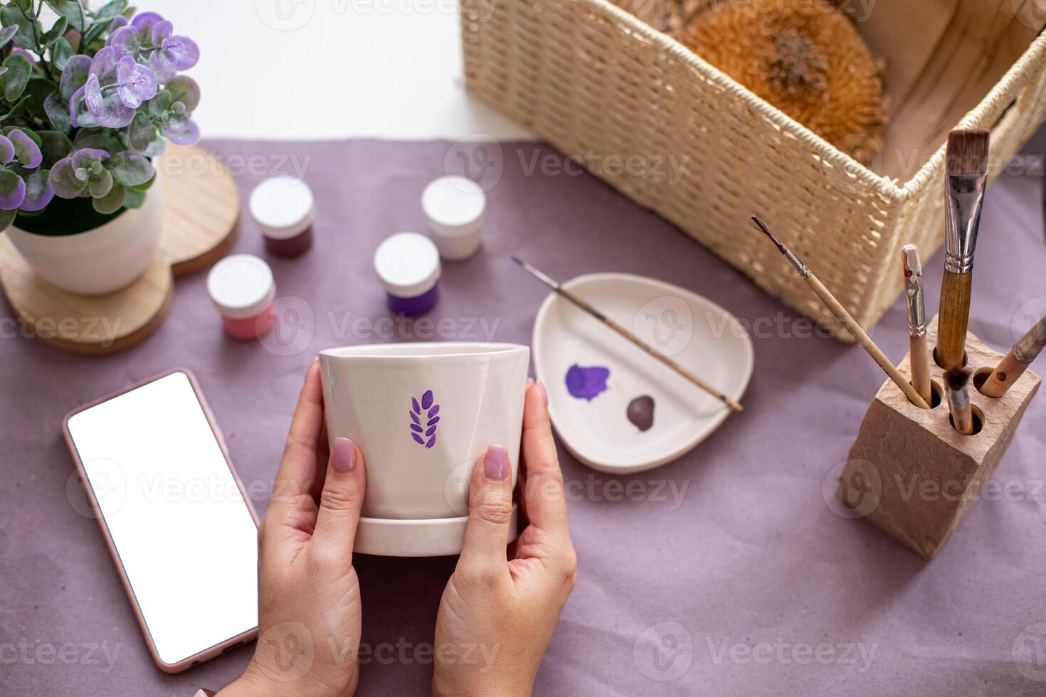 Womens hands hold a white flower ceramic pot on the table with craft tools photo
