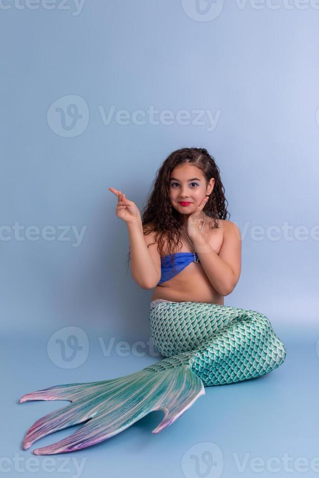A happy girl in a mermaid costume sits on a blue background photo
