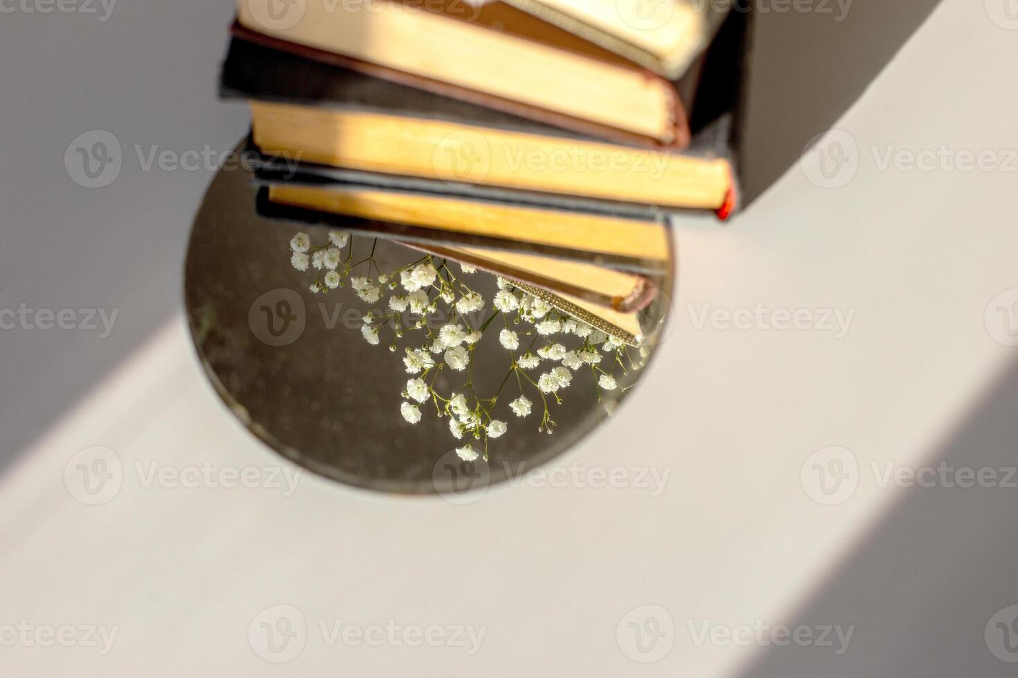 three old books lie with white gypsophila flowers and a round mirror on the table in the sunlight photo