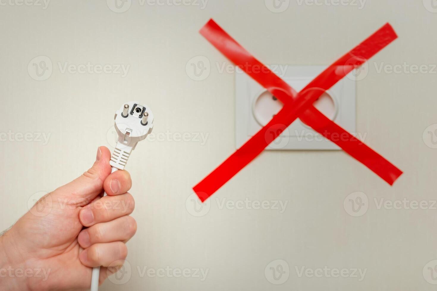 A mans hand holds a white cord near an electrical outlet, tied with a red ribbon crosswise. photo