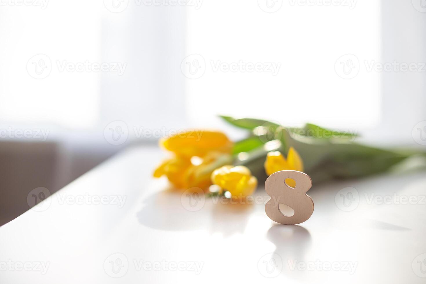 Wooden number eight and bouquet of yelow tulips stands on a white table. photo