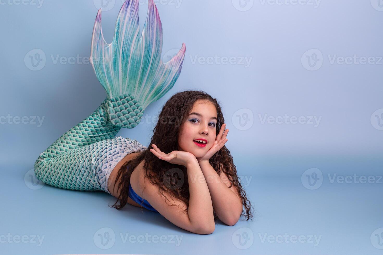 Adorable child girl in a mermaid costume lie isolated on light-blue background photo