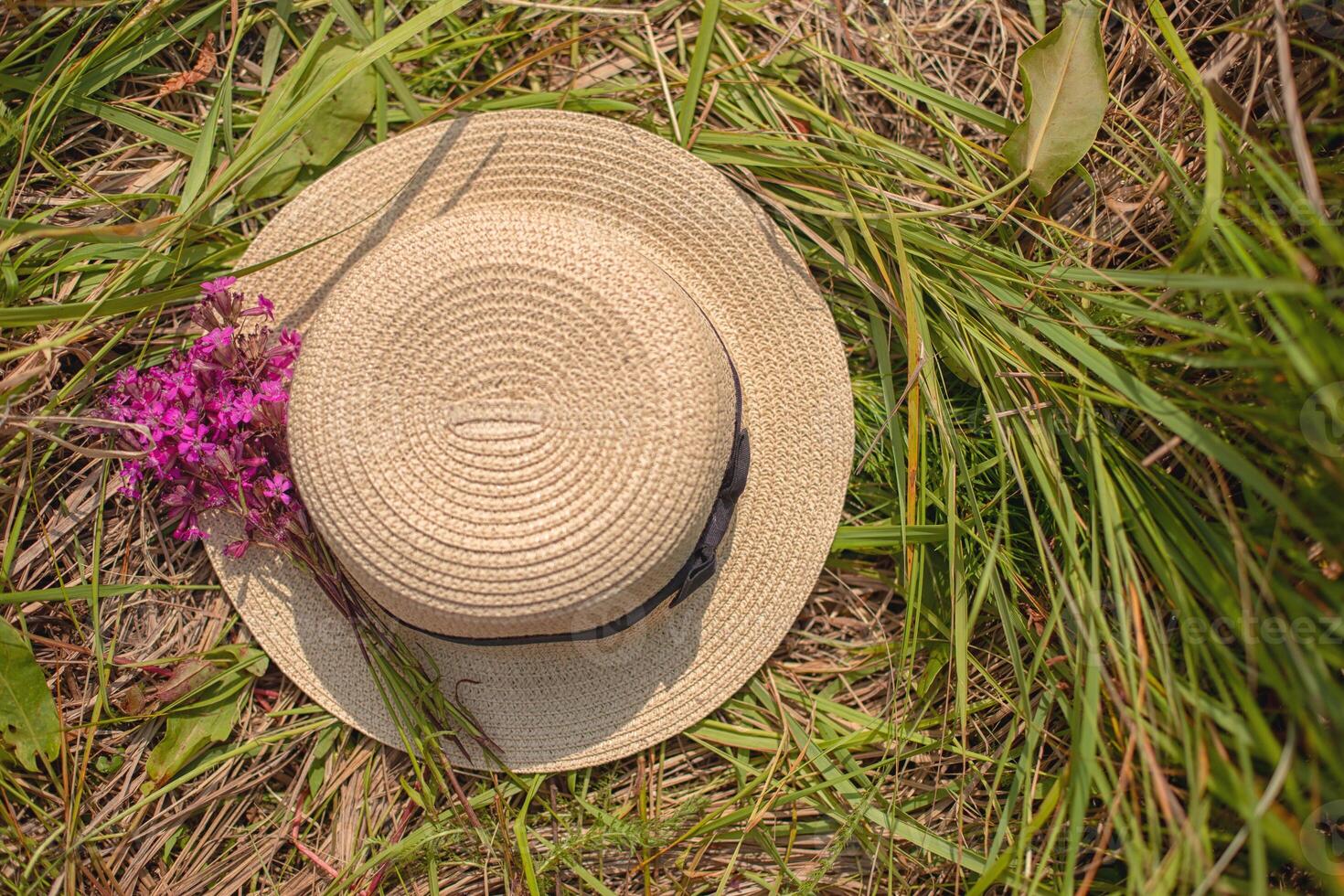 Straw Hat with a small bouquet of purple wildflowers on the green grass. photo