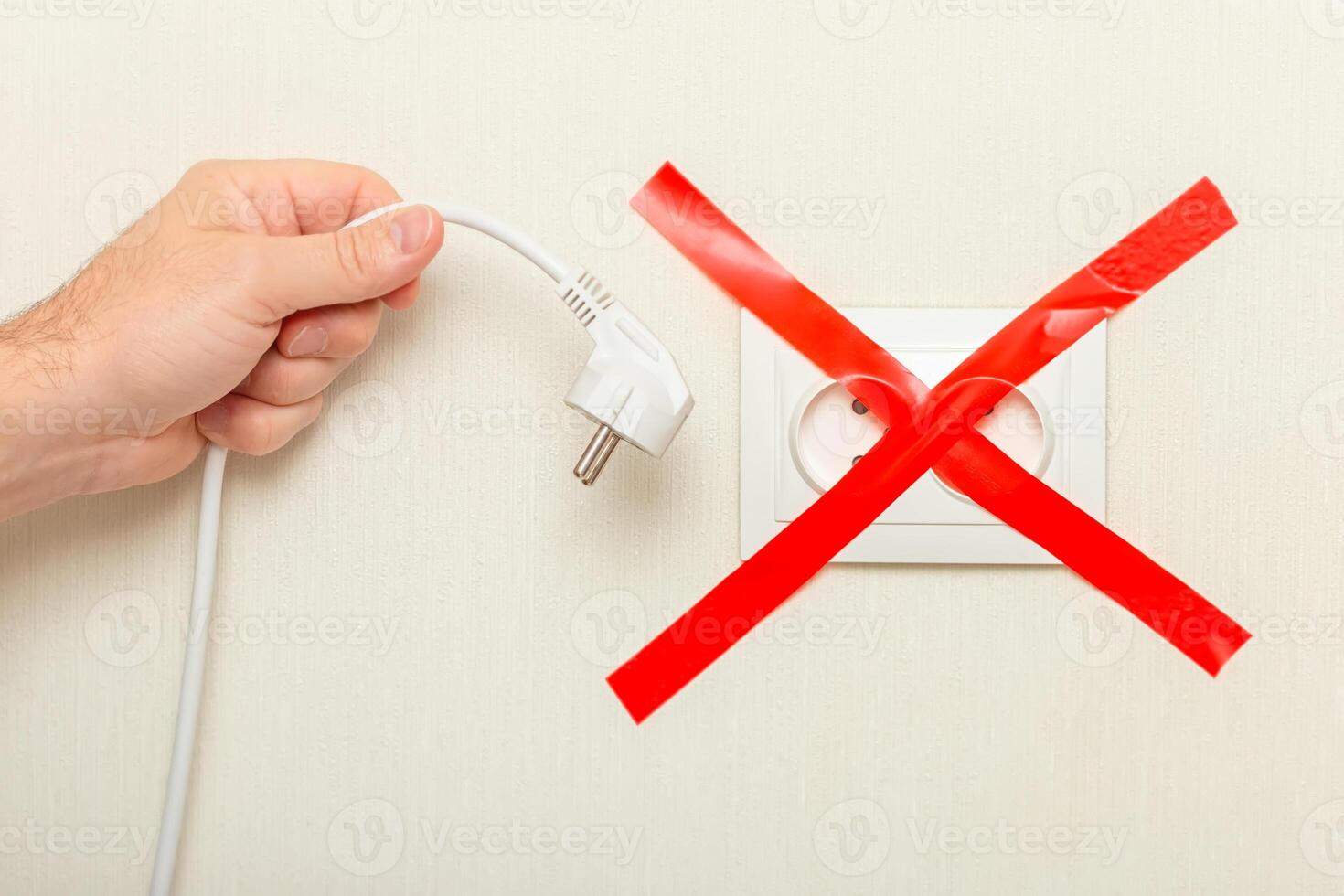 A hand holds a drooping white cord near an electrical outlet, tied with a red ribbon crosswise. photo