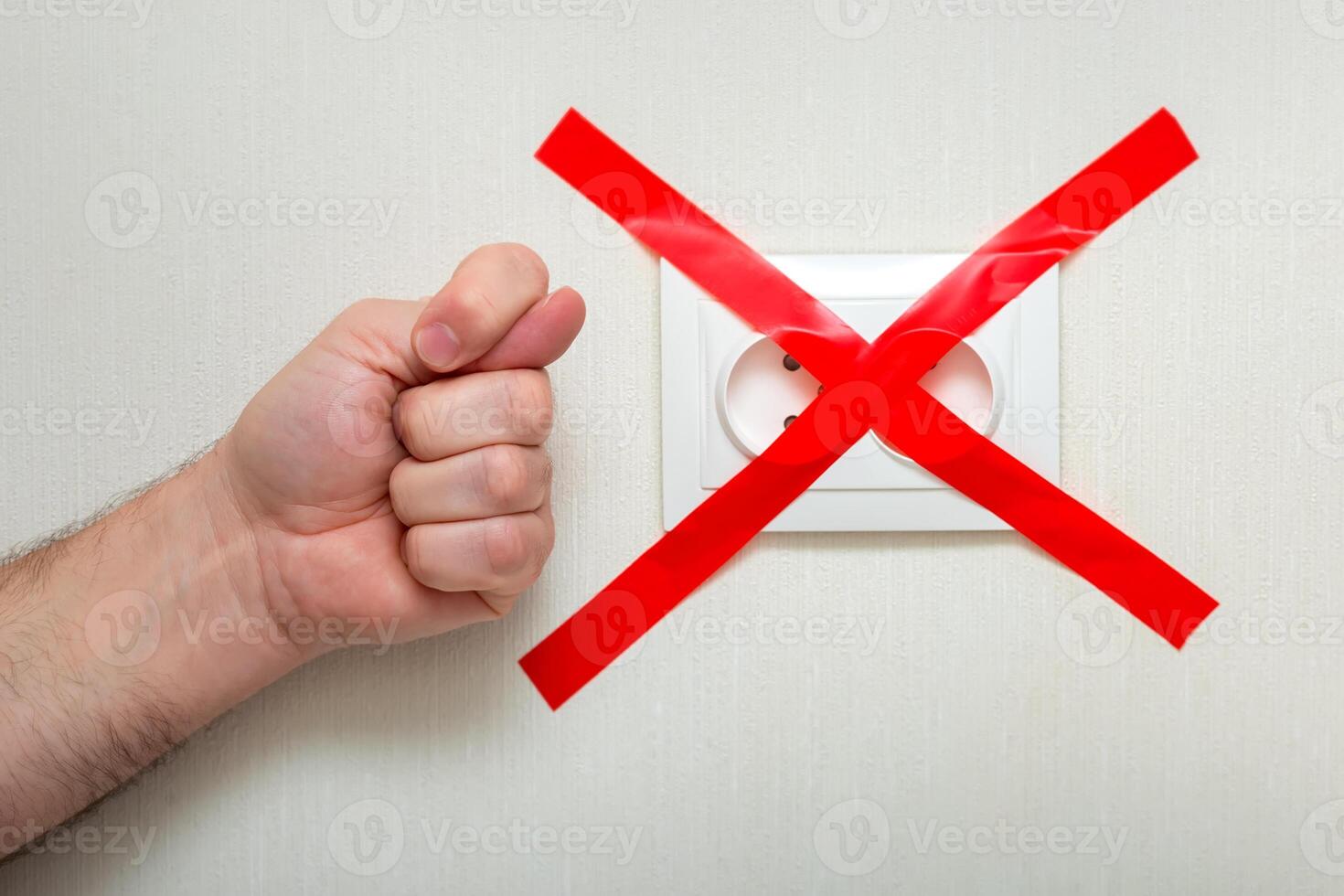 The man shows a fig gesture near the electrical outlet, tied with a red ribbon criss-cross. photo