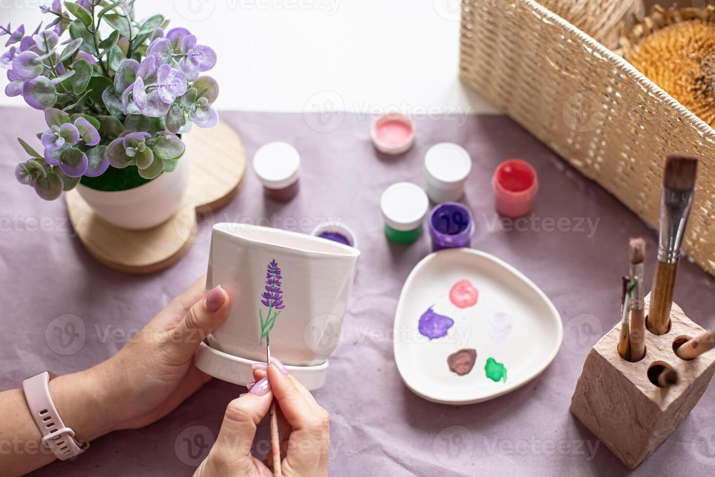 Womens hands paint a white flower ceramic pot on the table. Top view photo