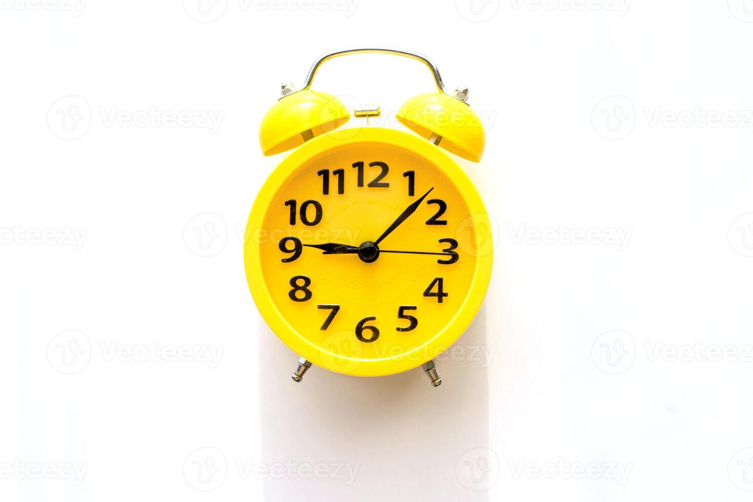 A yellow alarm clock with a black dial lies on a white table, top view photo