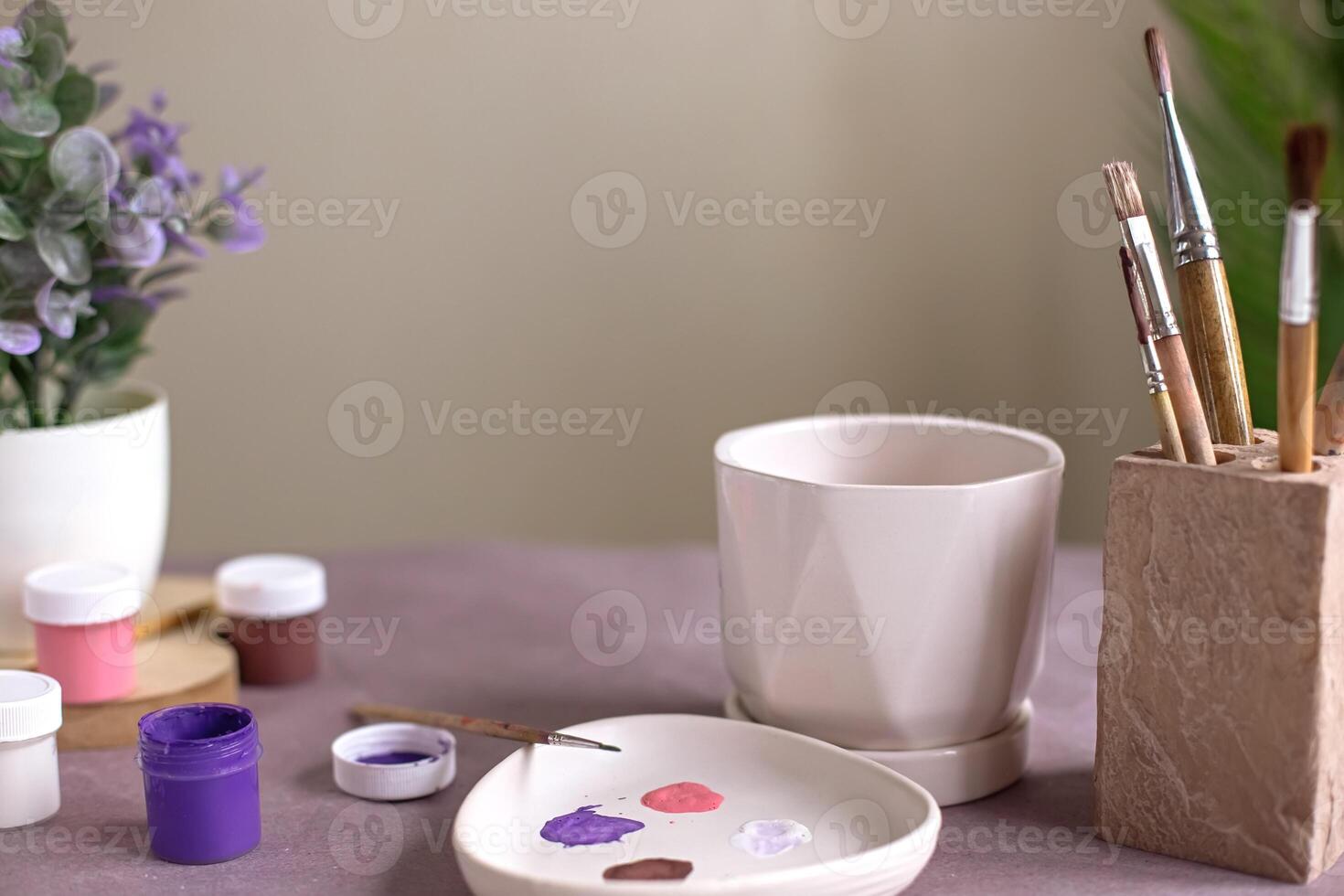 A still life with a white ceramic flower pot stands on a table with crafting tools photo