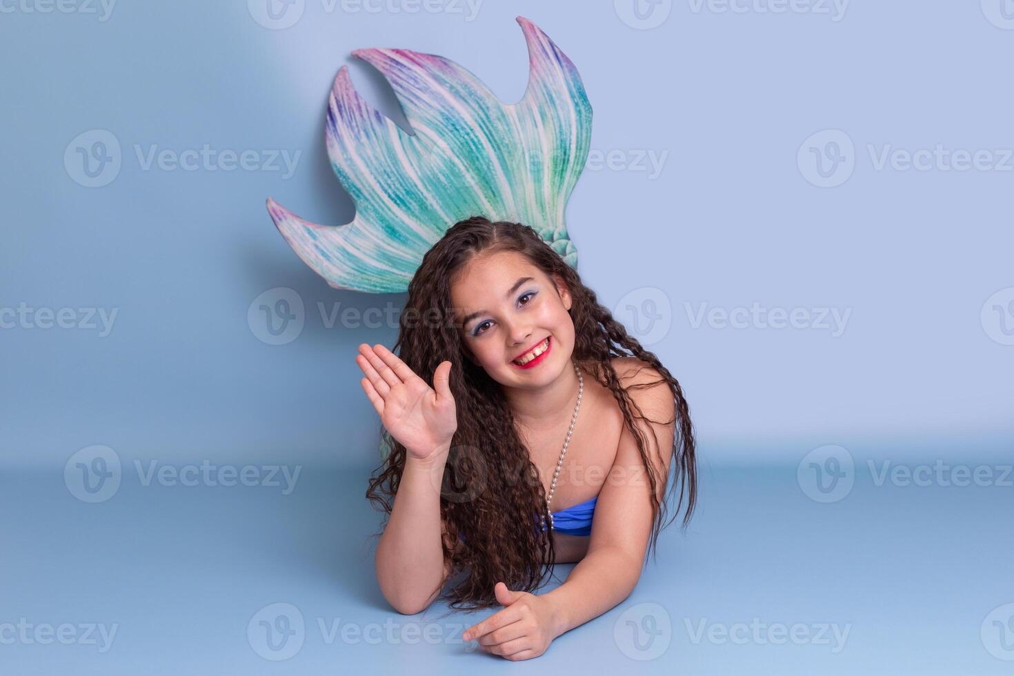Beautiful girl in a mermaid costume, friendly, lies on a blue background photo
