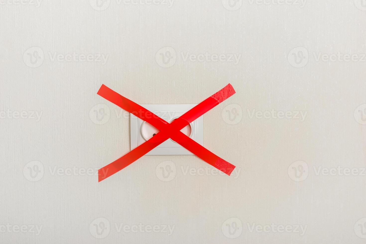 Electrical outlet, on a light wall, covered with a red ribbon cross to cross photo