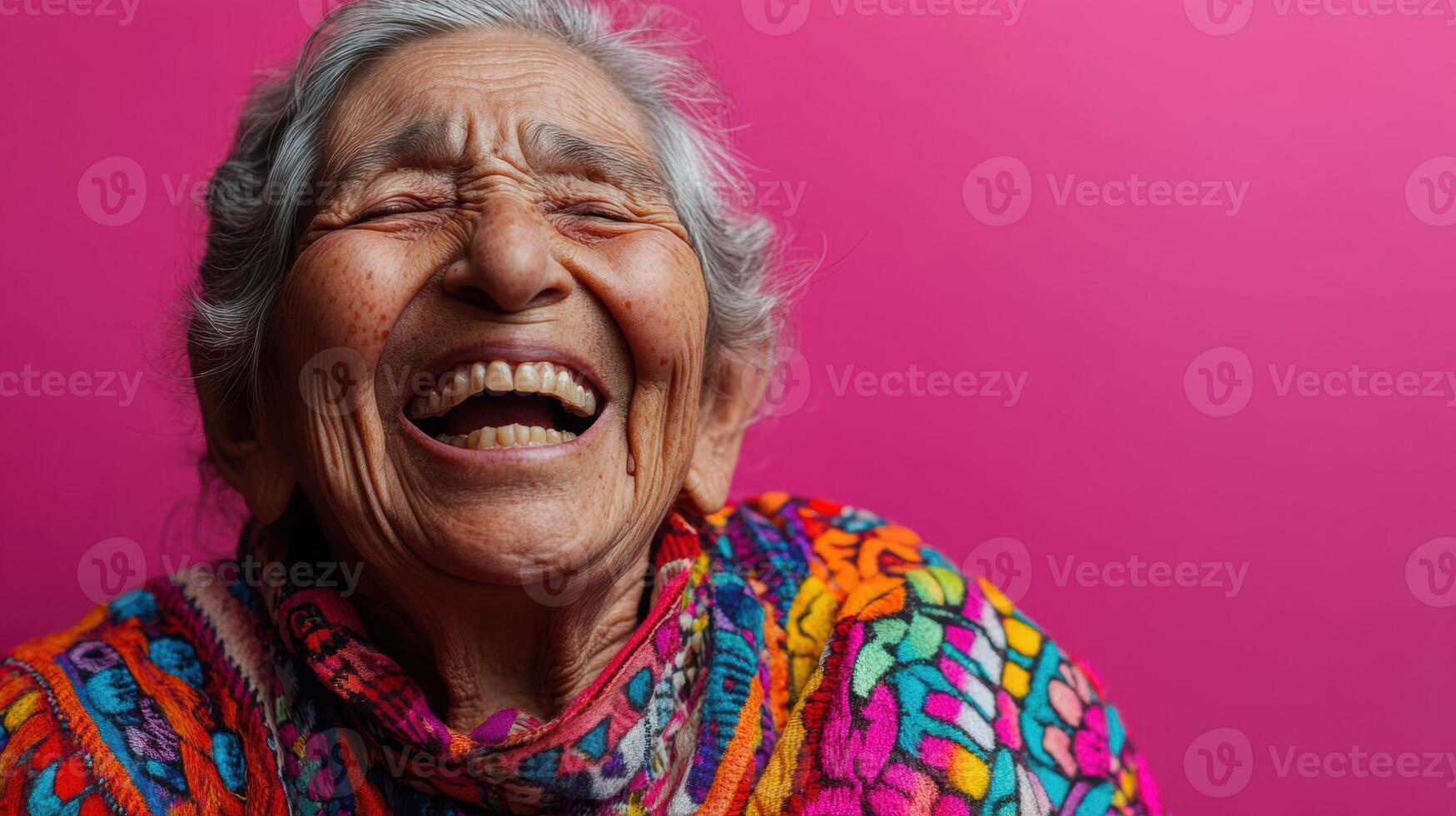 Close-up of a joyful elderly woman laughing heartily, wearing a colorful garment, expressing pure happiness and warmth against a bright pink background. photo