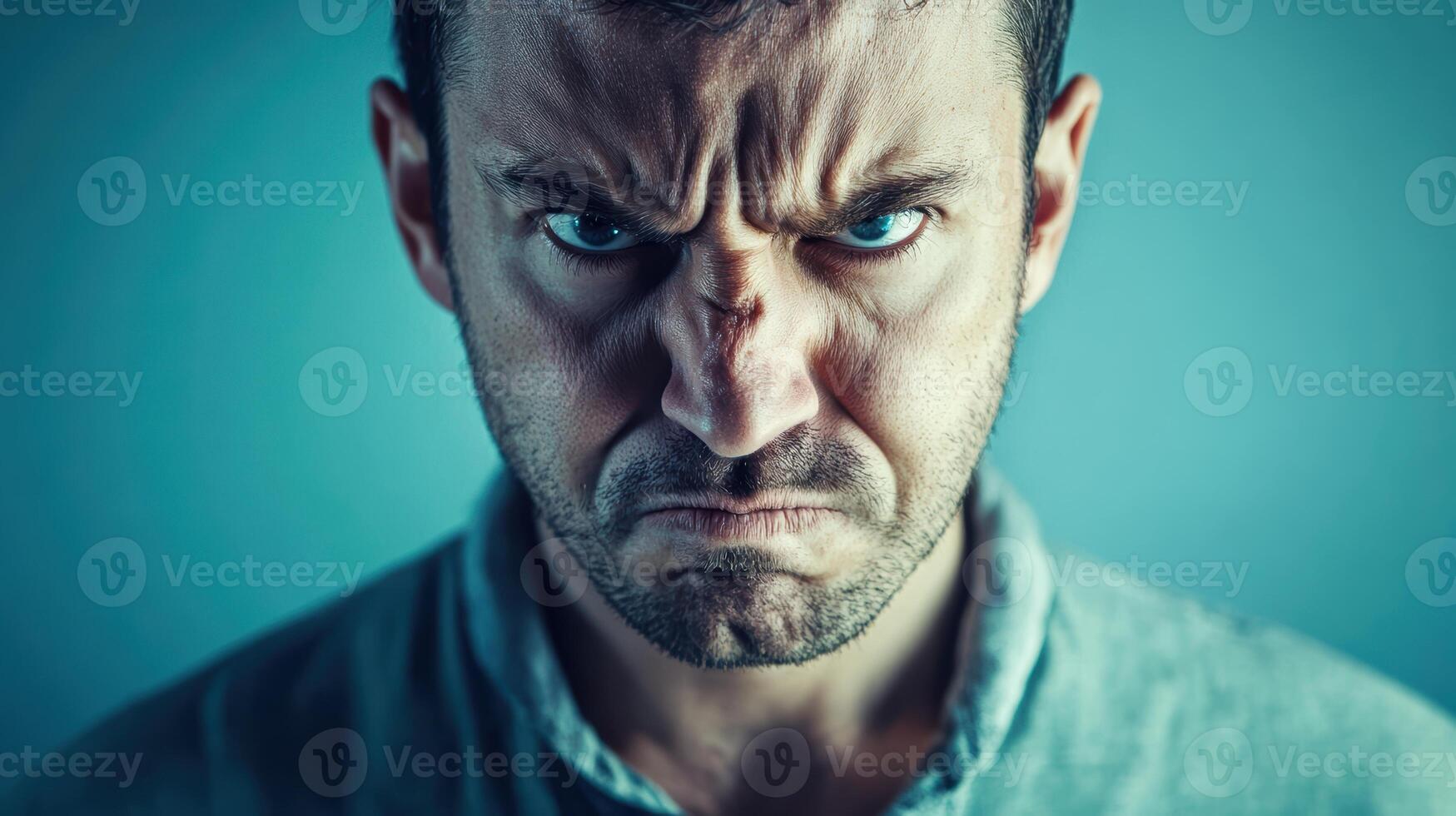 Close-up portrait of an angry man with a furrowed brow and intense expression, glaring directly at the camera against a plain background. photo