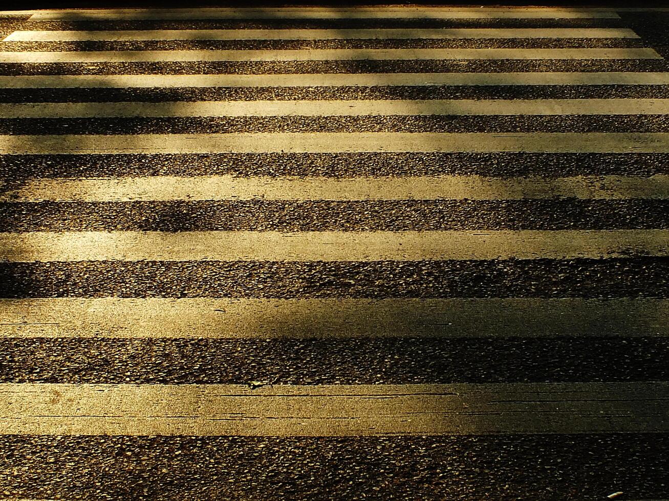 A road with a zebra crossing. The stripes are faded and the road is covered in gravel photo