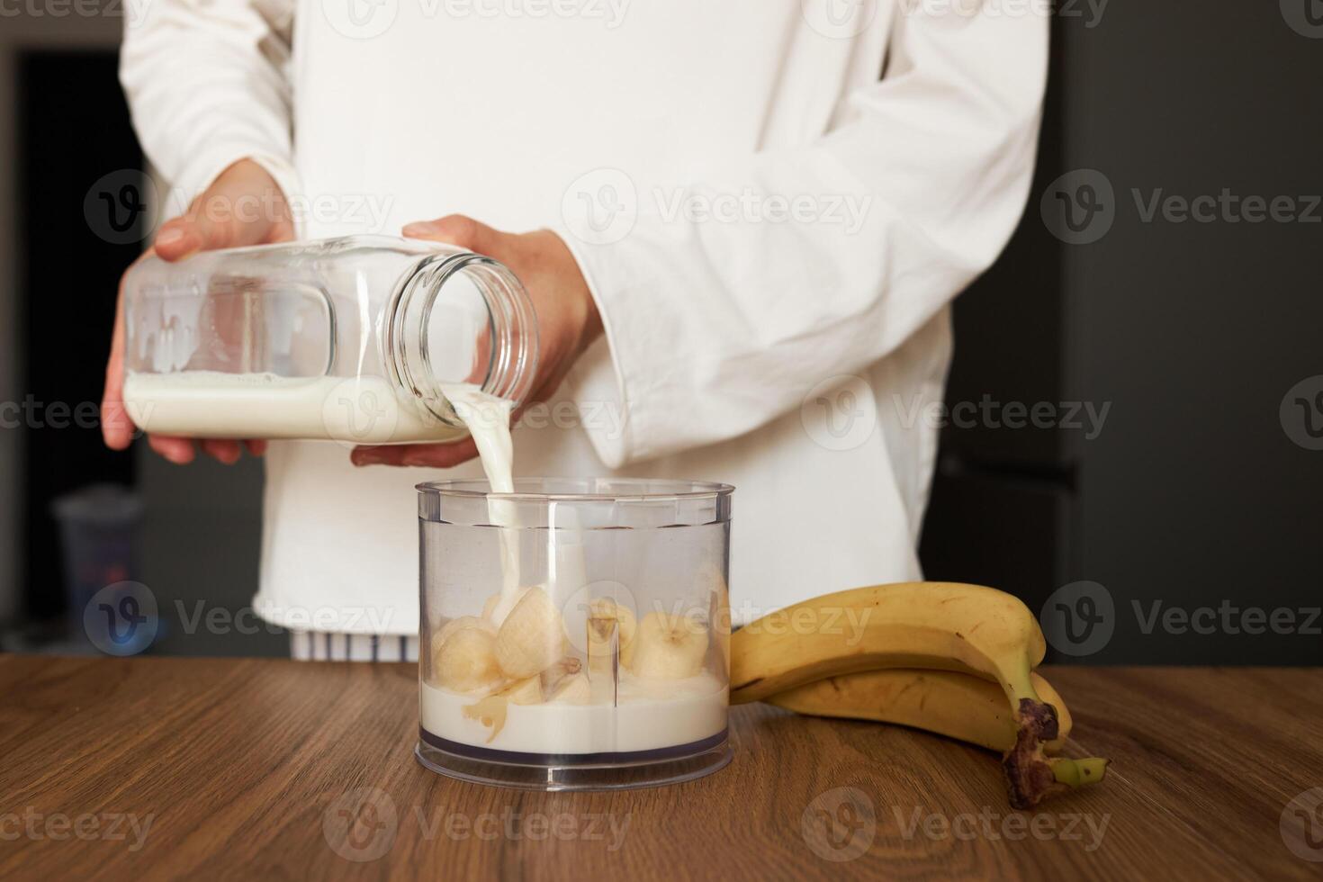 Woman preparing an healthy smoothie with bananas, she is pouring milk into a blender photo