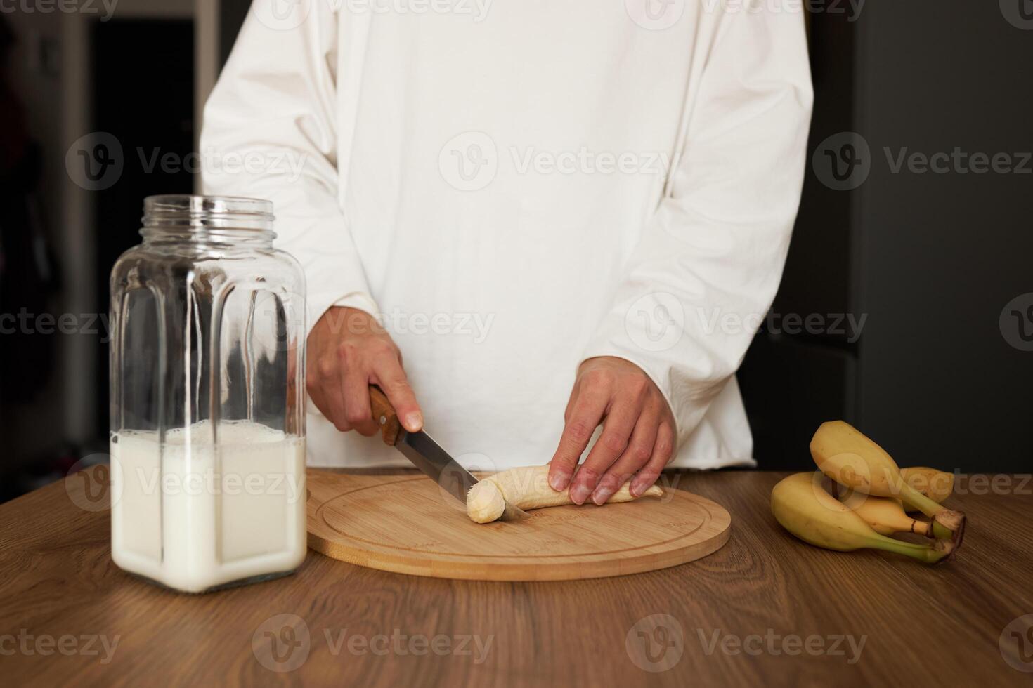 Close up of young woman with blender chopping banana for milkshake at home photo