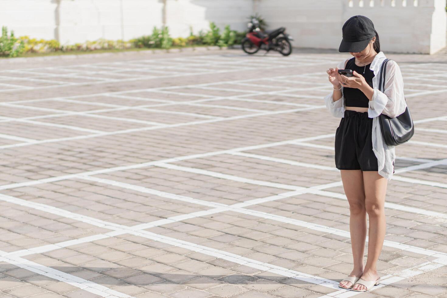 A woman in a hat and shorts is looking at her phone photo