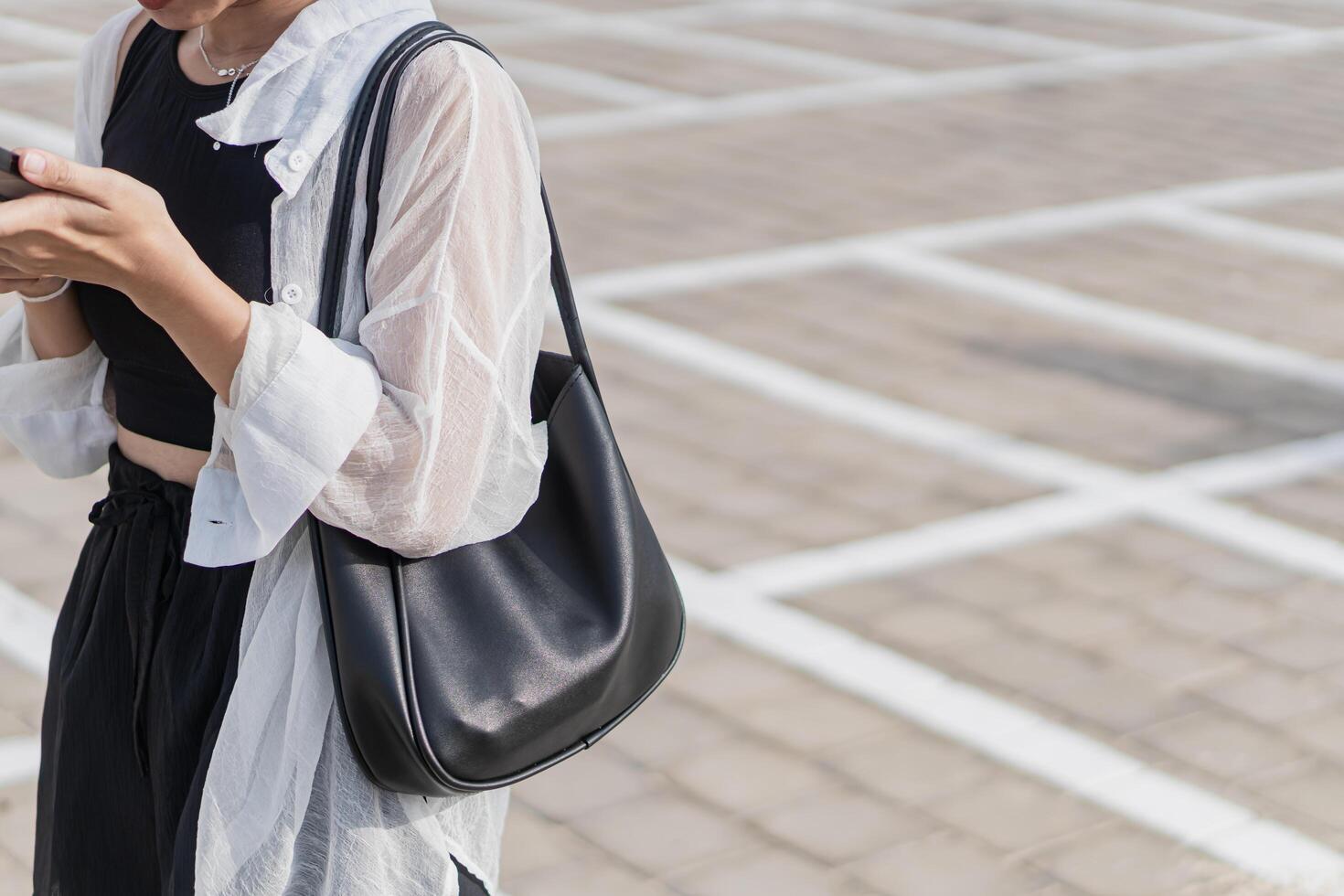 A woman in a black skirt and white shirt looking at her phone photo