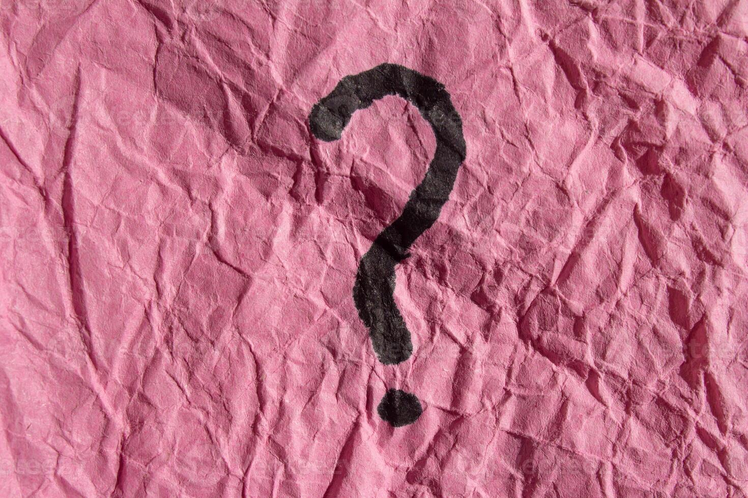 A question mark is drawn on a pink piece of paper photo