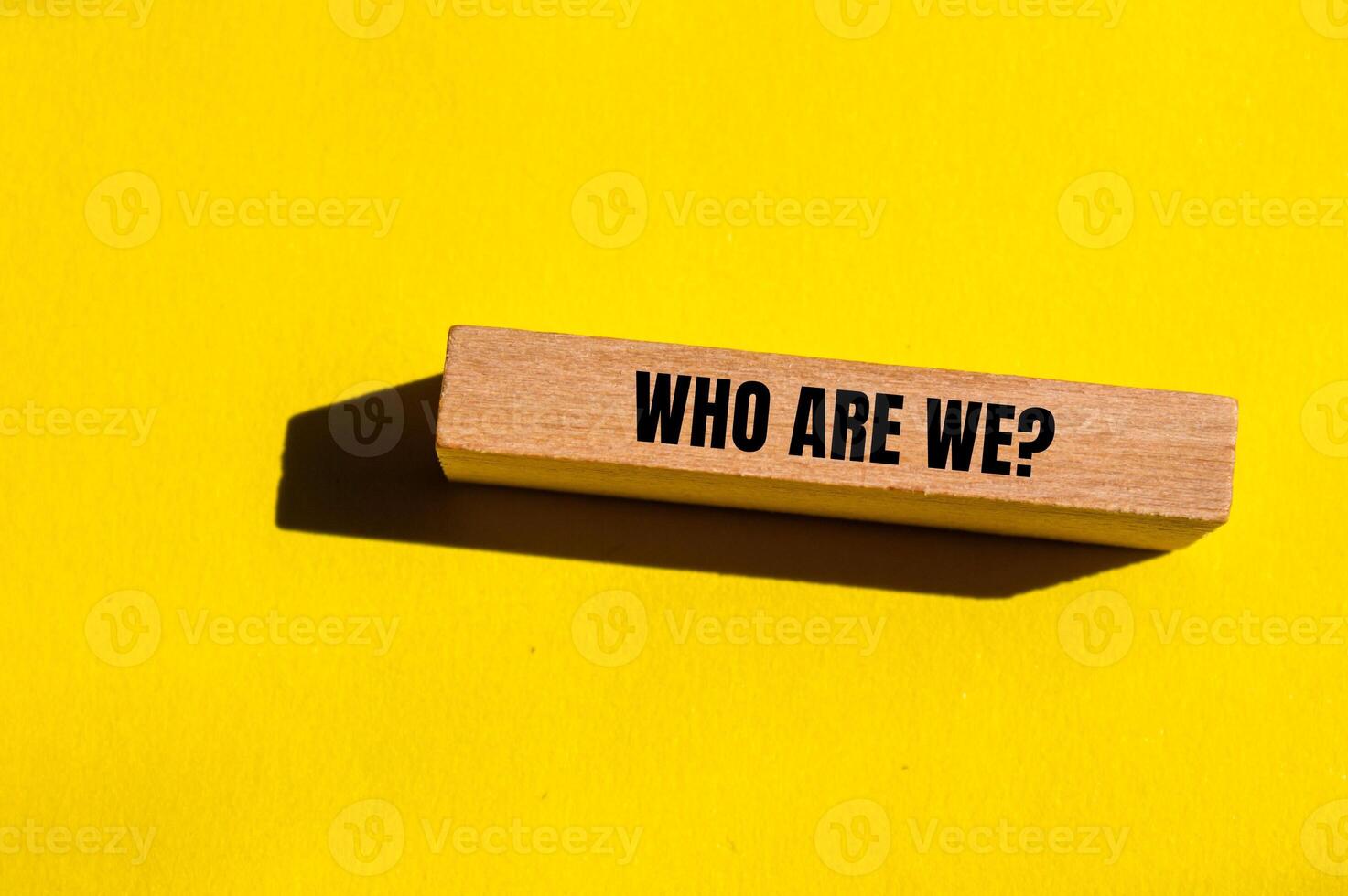 Who are we question written on wooden block with yellow background. Conceptual who are we question symbol. Copy space. photo