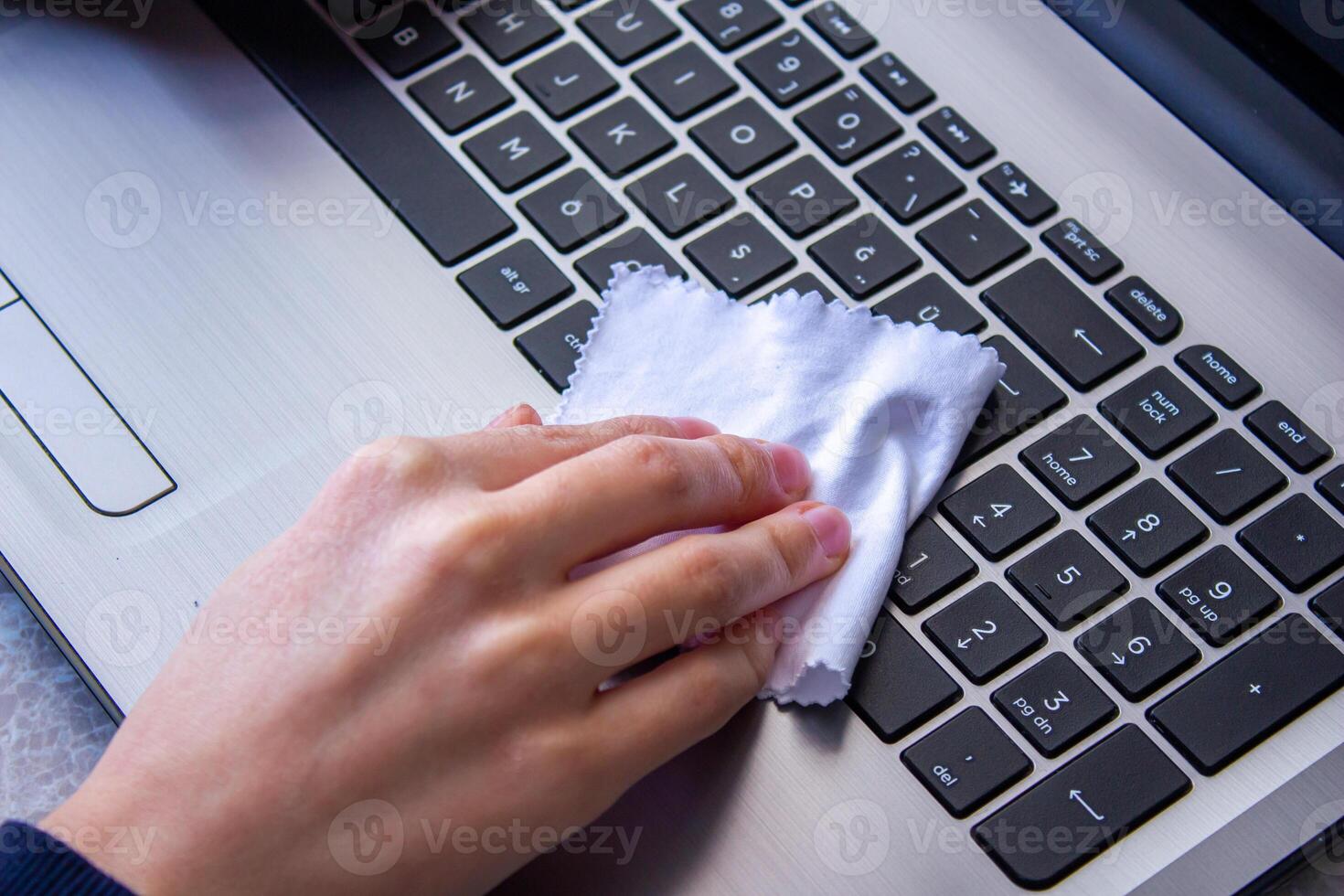 A person cleaning a laptop keyboard with a cloth photo