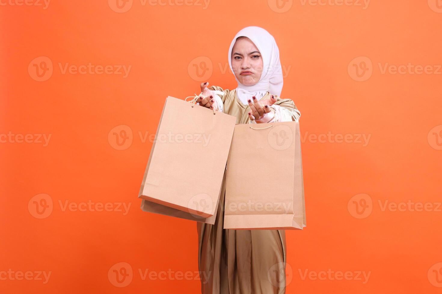 Young indonesia woman sullenly carries a brown paper bag to the front containing shopping items wearing a kaftan Muslim dress with a hijab. Fashion concept, transaction, promotion photo