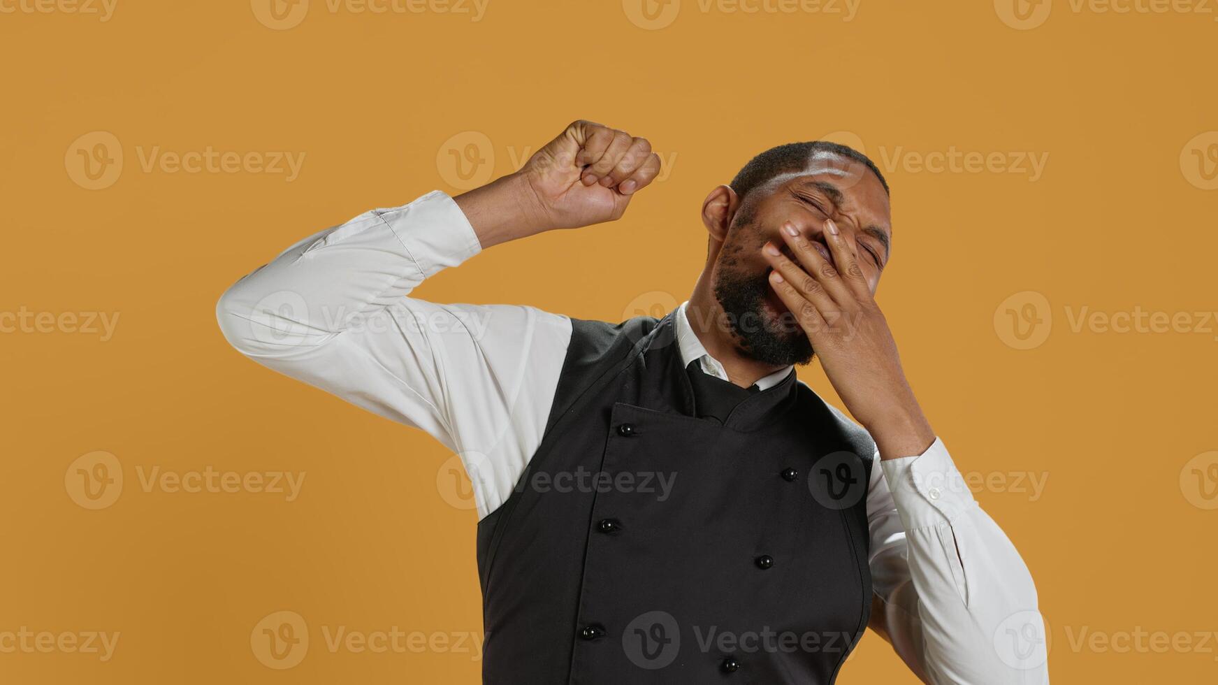 Tired waiter yawning and stretching after a night shift and feeling exhausted, sleepy employee falling asleep in studio. Hospitality industry staff works in customer service, burnout. Camera A. photo