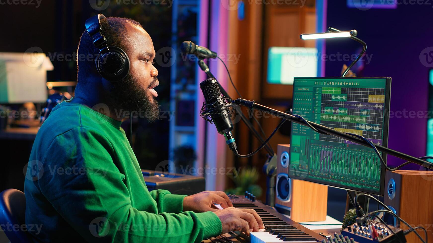 Artist recording new tracks by playing piano notes on electronic keyboard in his home studio, working with audio stereo gear to mix and master tunes. African american musician. Camera A. photo