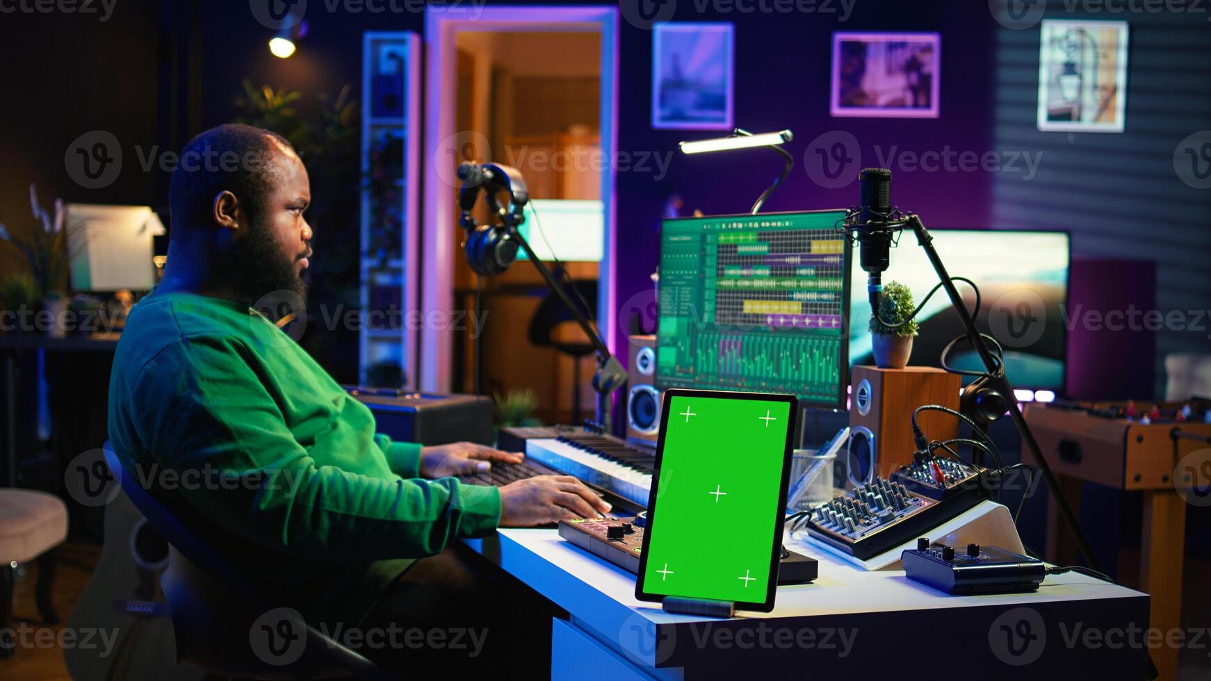 Composer editing his audio files and recordings on daw software, sitting next to a green screen display. Skilled sound technician uses mixing and mastering gear to produce new material. Camera B. photo
