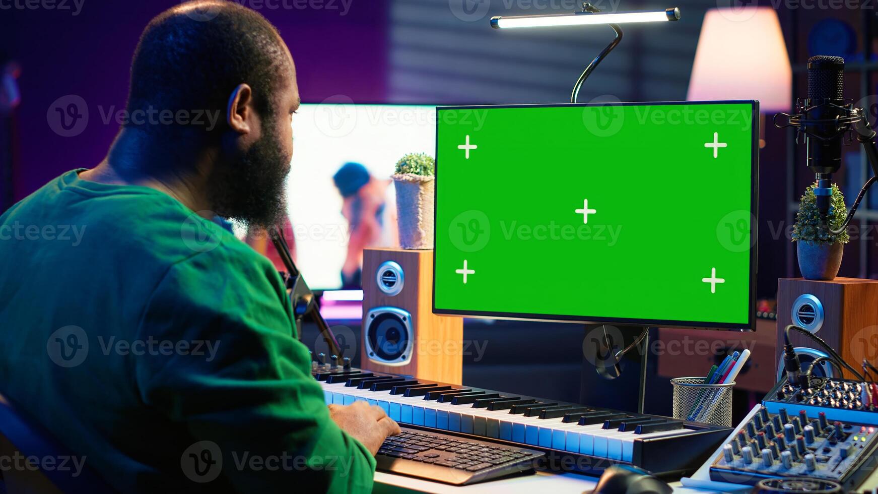 Producer composing music with electronic keyboard notes and green screen display on pc, post production in home studio. Musician artist plays midi controller next to mockup layout. Camera A. photo