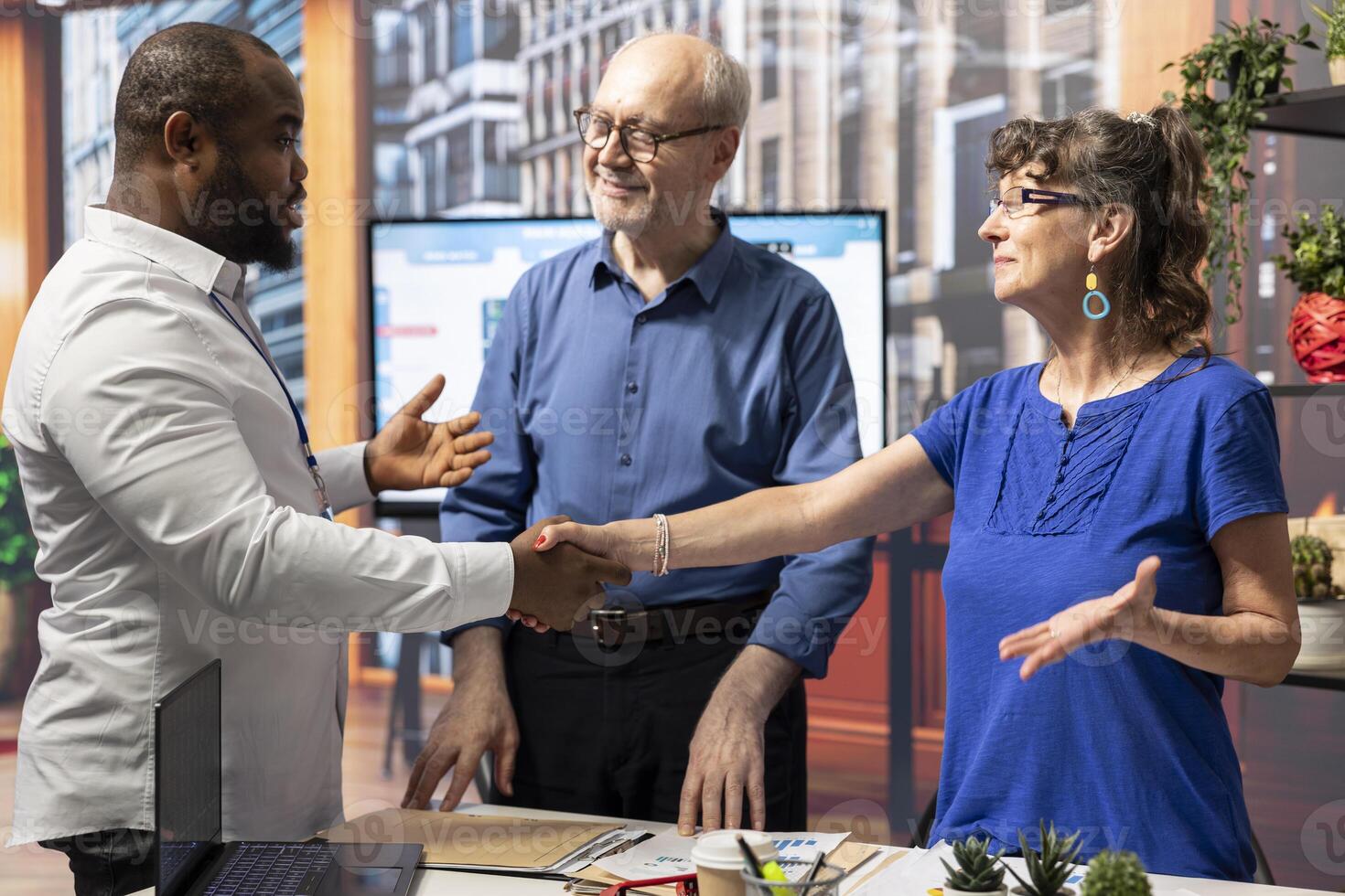 Senior citizens shaking hands with a financial advisor after discussing retirement plans and securing their financial future. Fruitful counseling meeting with senior clients in office. photo