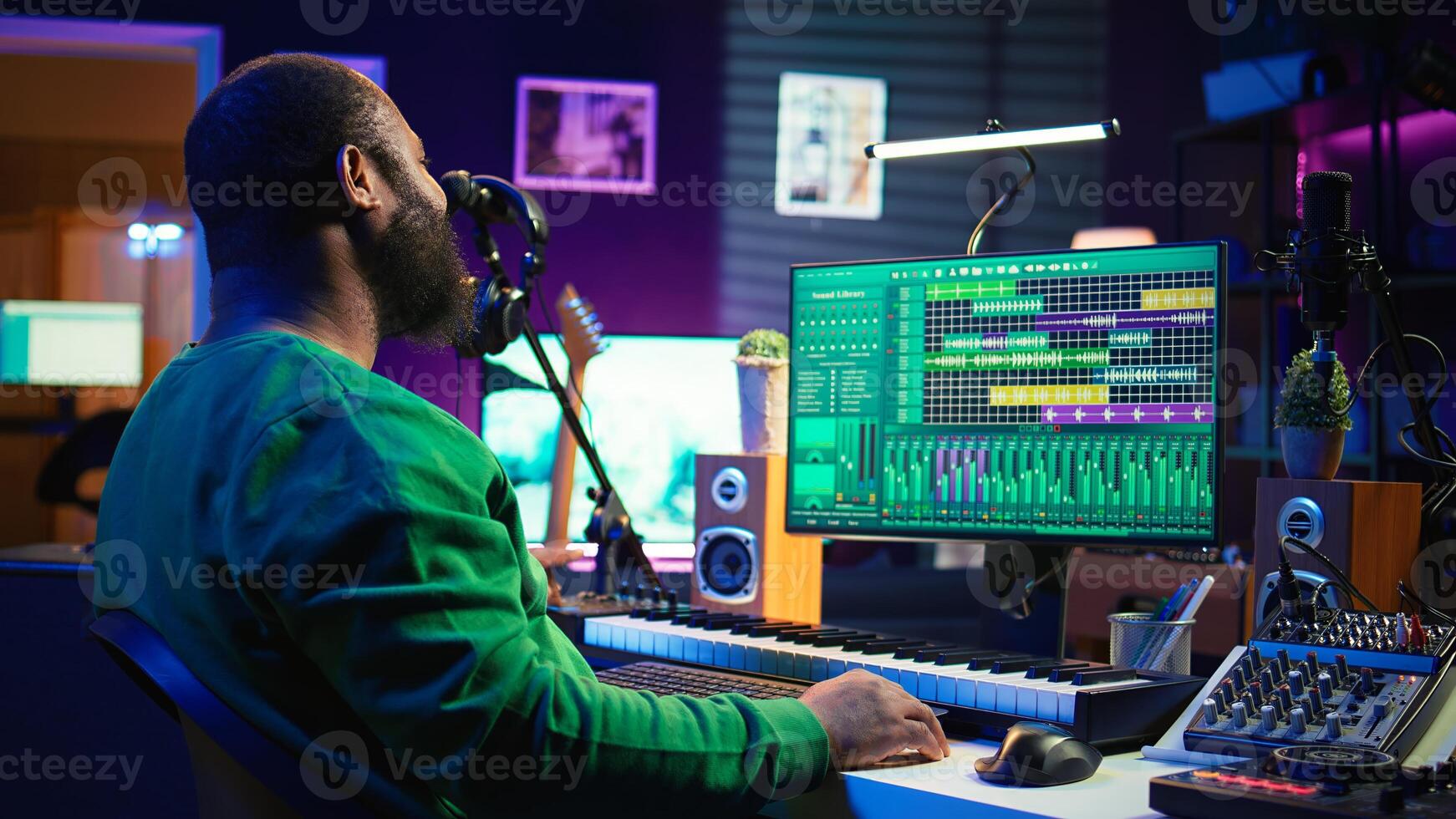 African american artist composing a new soundtrack for a project, using professional production software in home studio. Skilled creative singer producing music and adding sound effects. Camera B. photo
