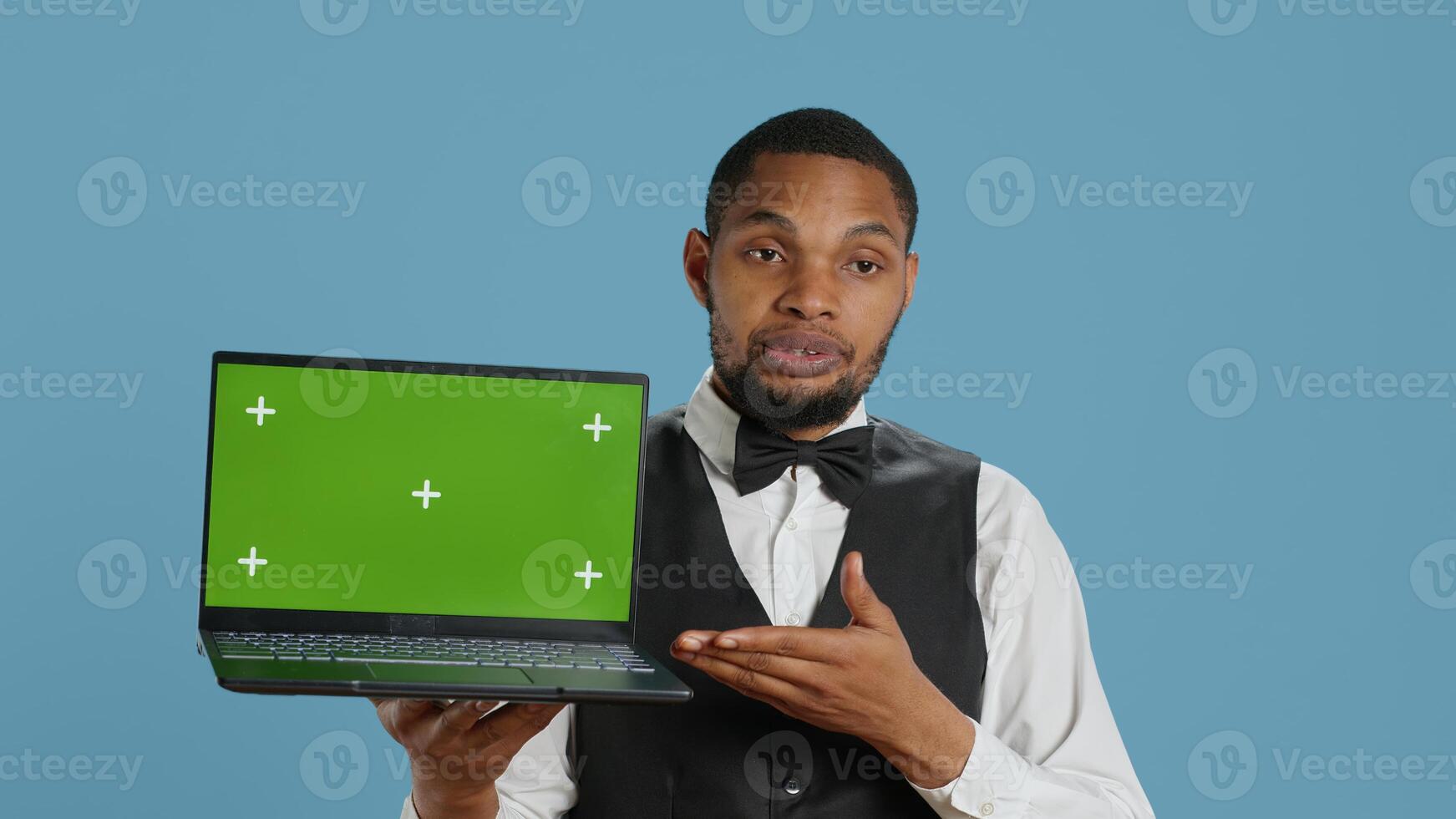 Doorkeeper bellboy holding a laptop with green screen in studio, presenting isolated chroma key display while he works in hospitality industry at a five star hotel. Professional staff. Camera A. photo