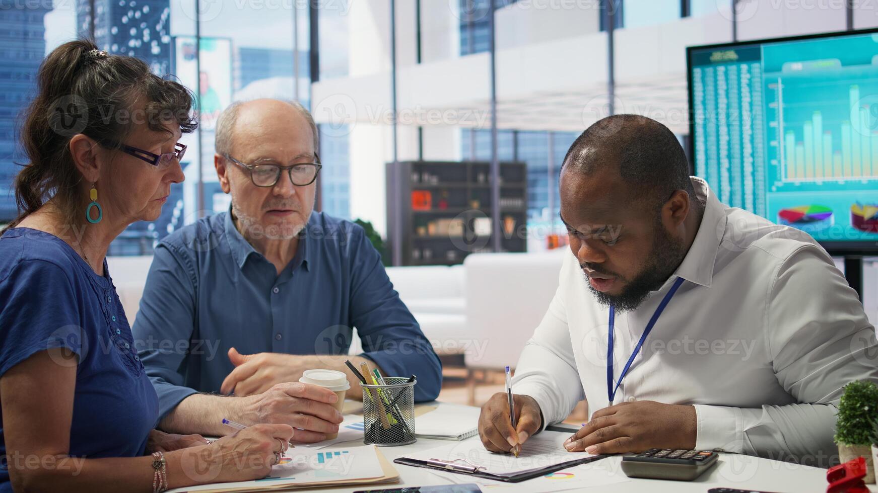 Senior citizens consulting a broker to explore pension options, ensuring their savings and investments are optimized for the future. Meeting with financial expert about retirement savings. Camera B. photo