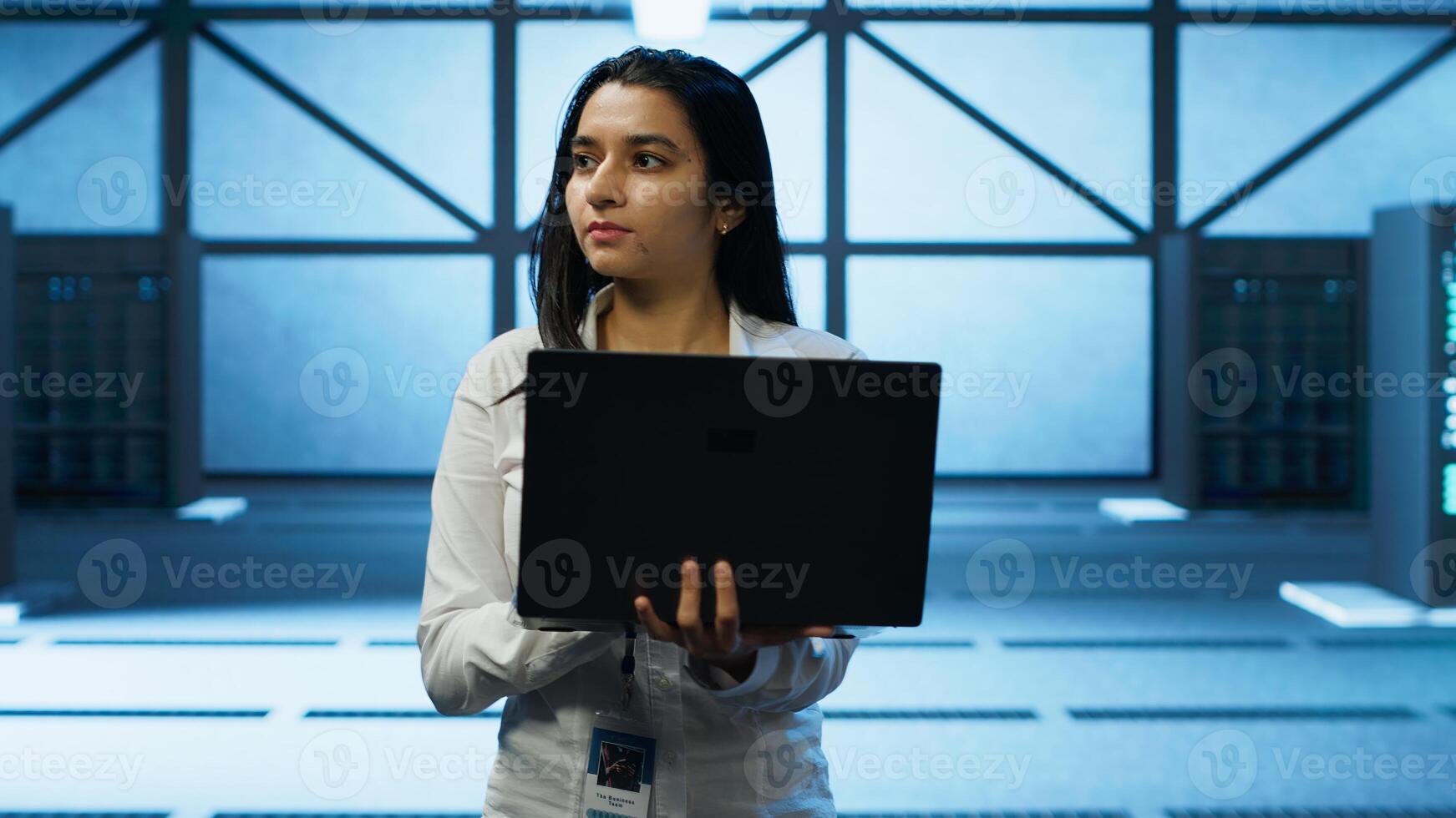 Programmer walking in data center, using notebook to design, implement and manage gear, ensuring optimal performance and reliability. IT professional in server hub coding on laptop, camera A photo