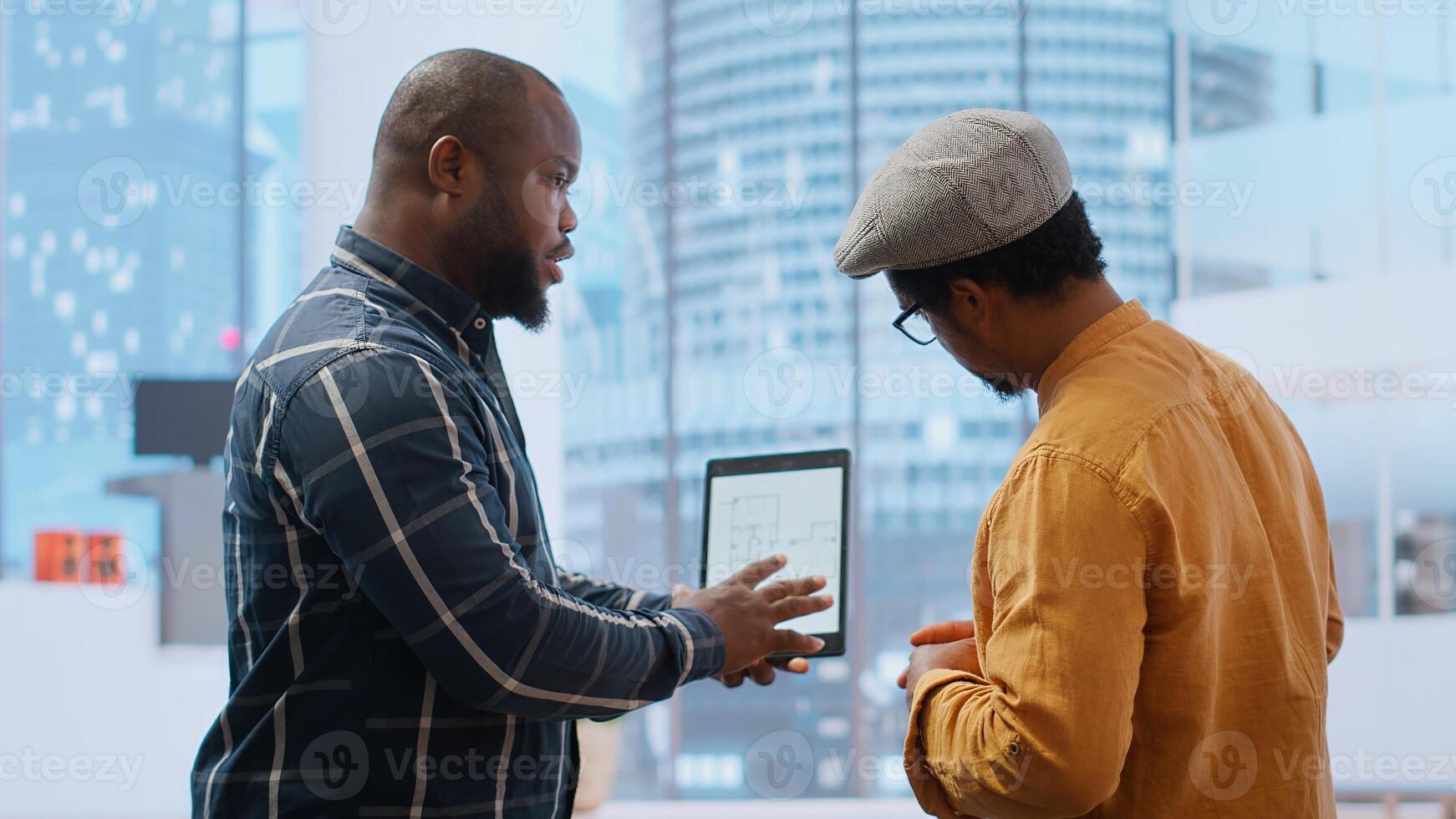 Real estate broker and client negotiating a leasing contract for a high class modern office space, evaluating blueprints on tablet during office tour. Property investment opportunity. Camera B. photo