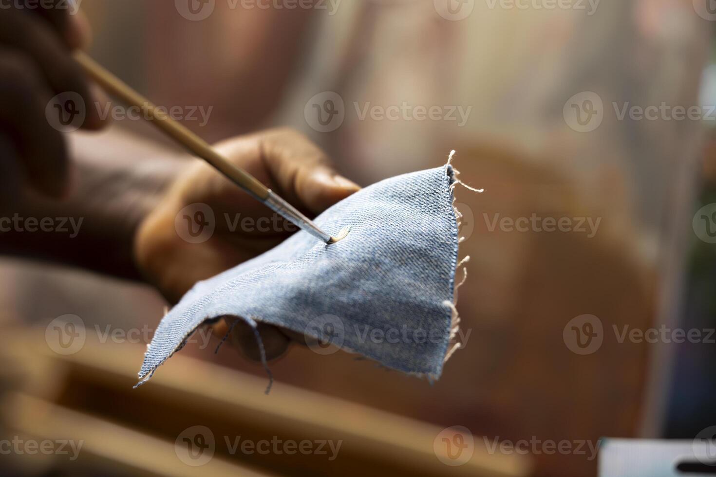 Talented artist cleaning the paintbrush on a piece of denim fabric from old dye colors, applying a different shade on canvas. Young man working hard on his new artistic masterpiece. Close up. photo