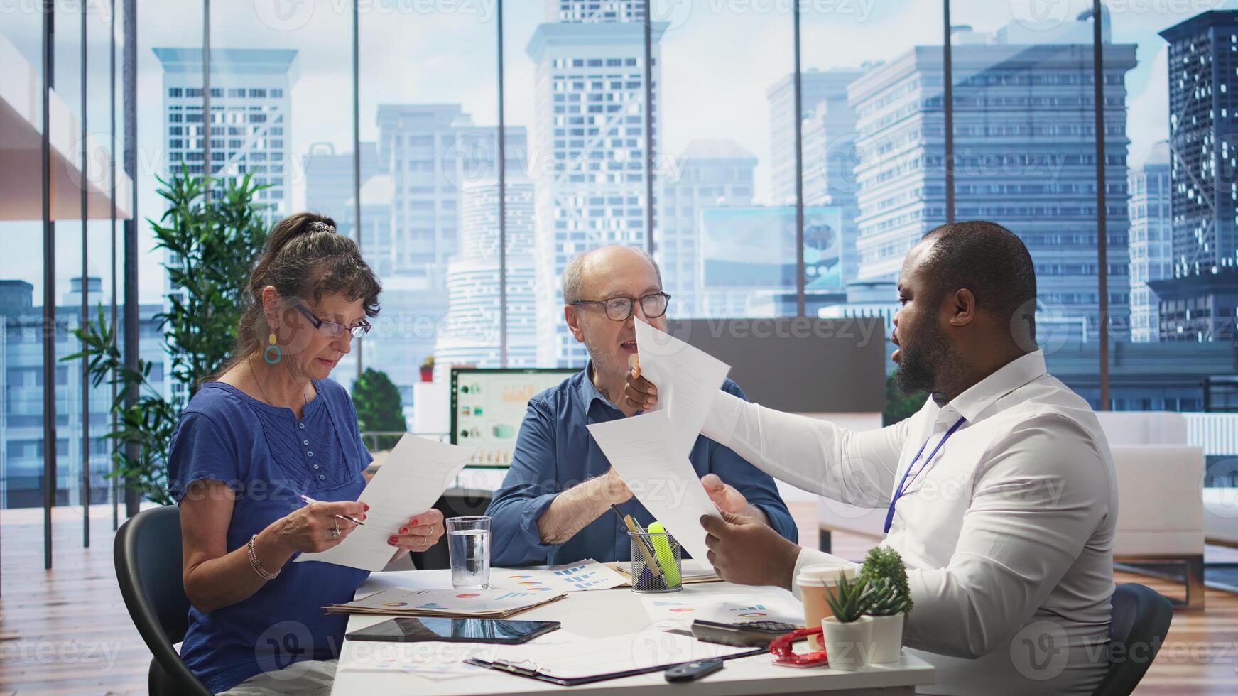 Mature couple meeting with a financial expert to develop a detailed retirement plan, focusing on savings and long term financial security. Clients discussing with broker in office. Camera B. photo