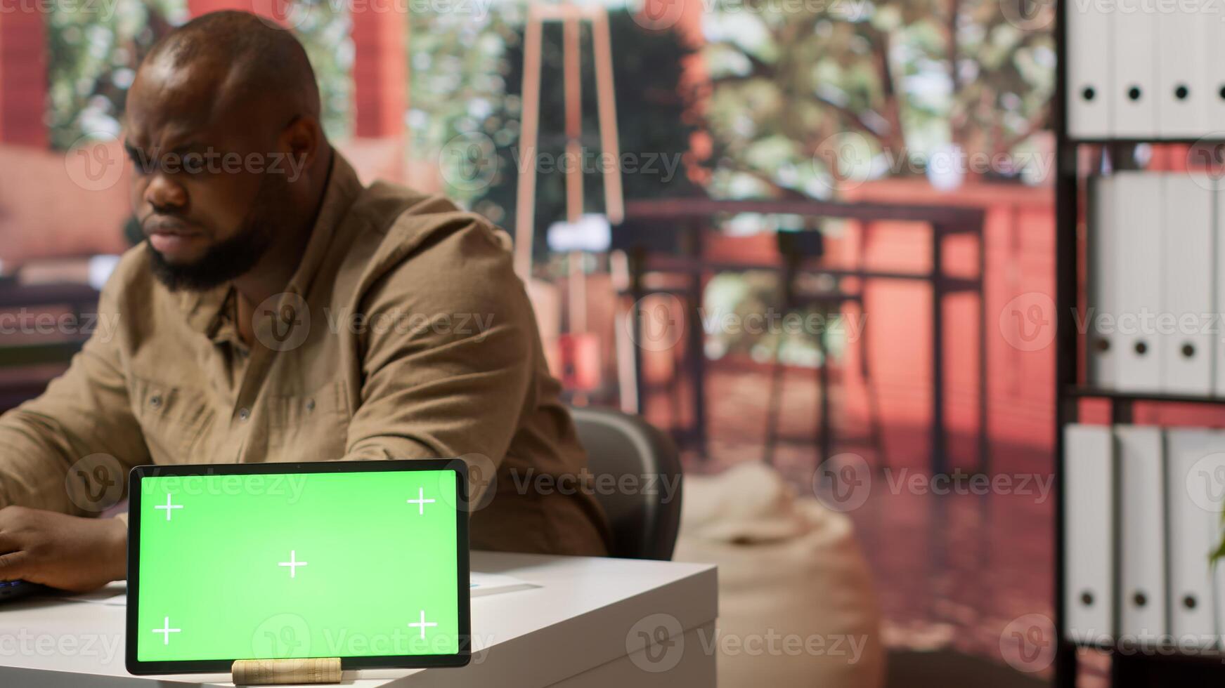 Businessman examines annual sales reports on documents next to a green screen tablet display, doing an accounting analytics plan. Entrepreneur working remotely from home office. Camera A. photo