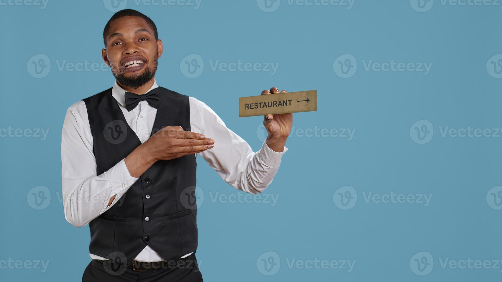 Doorman bellhop showing the restaurant direction with a hotel sign, holding an indicator to point guests to the amenities. Professional hotel concierge using a wall mark. Camera B. photo