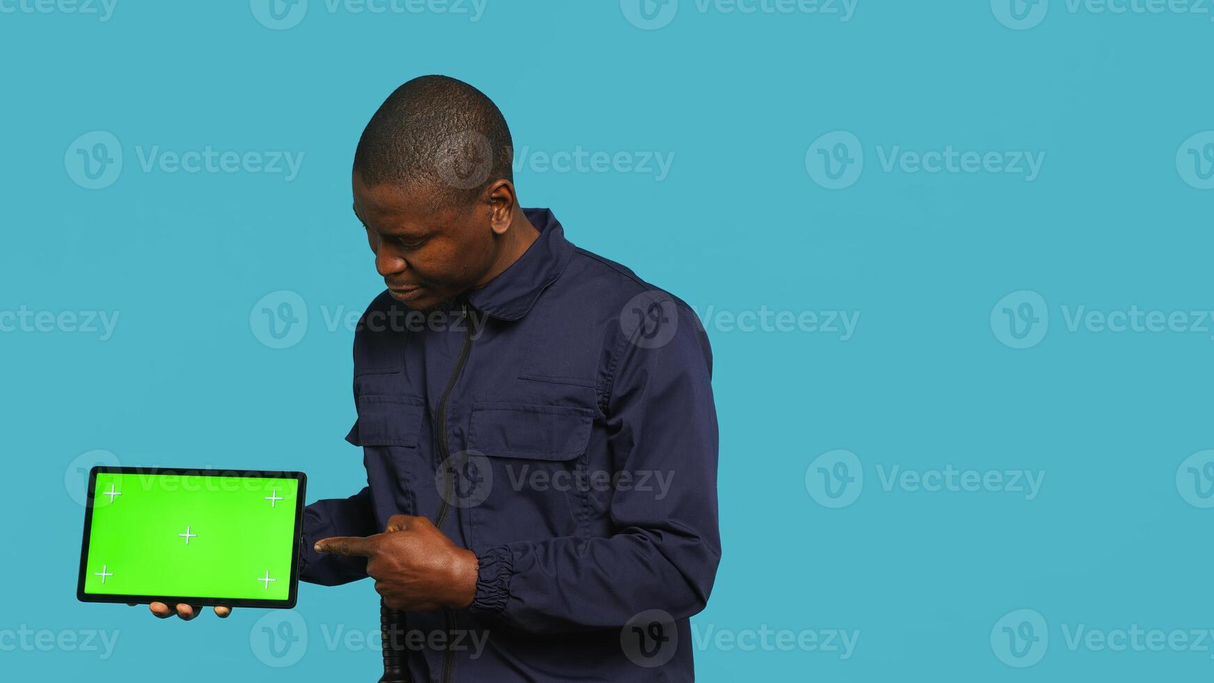 Portrait of smiling security guard at work showcasing isolated screen tablet while overseeing premises. Joyful private law enforcement worker presenting chroma key device, studio backdrop, camera A photo