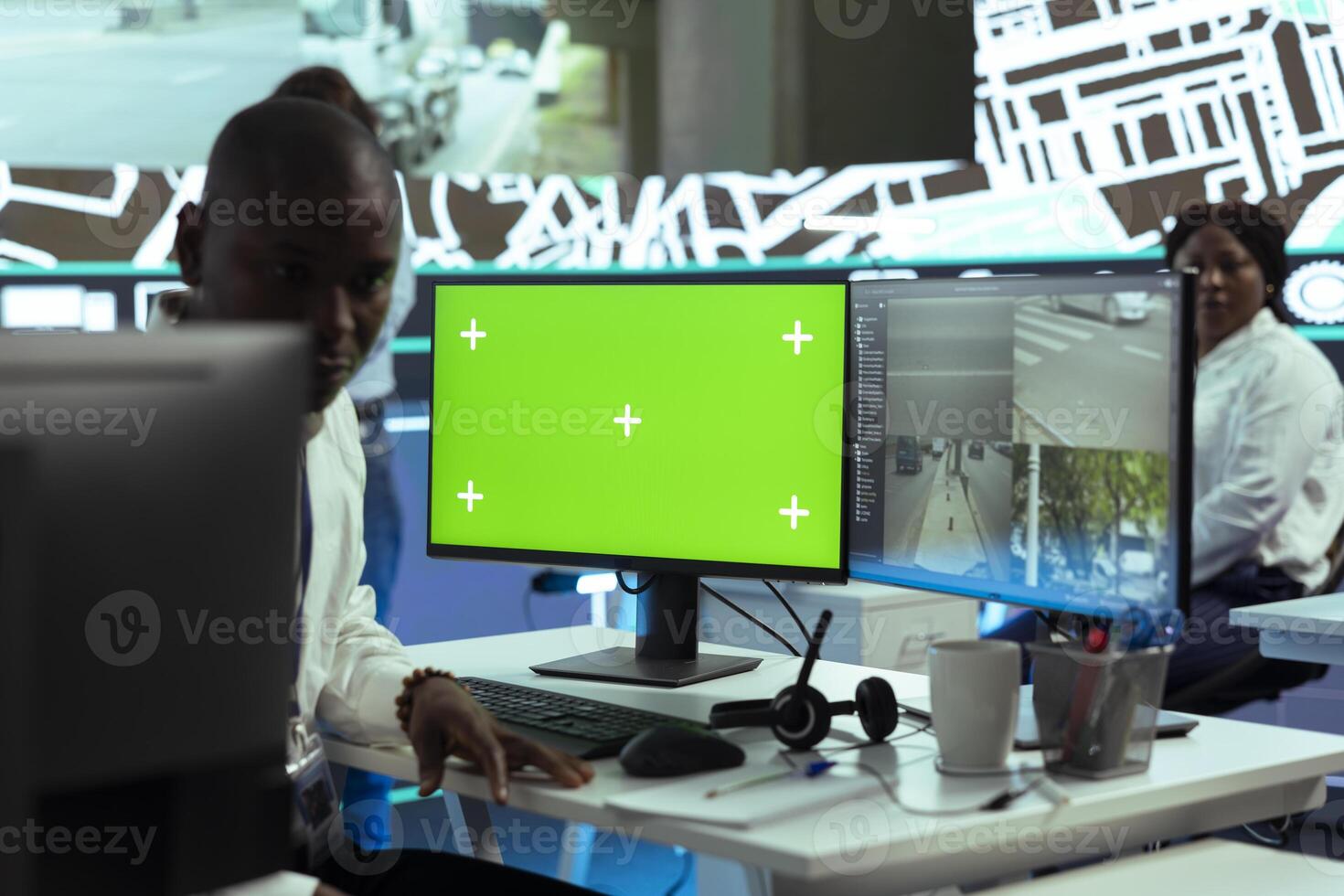 African american employee operates on CCTV footage and greenscreen display, ensuring express delivery in monitoring room control center. Male dispatcher following the cars in traffic. photo