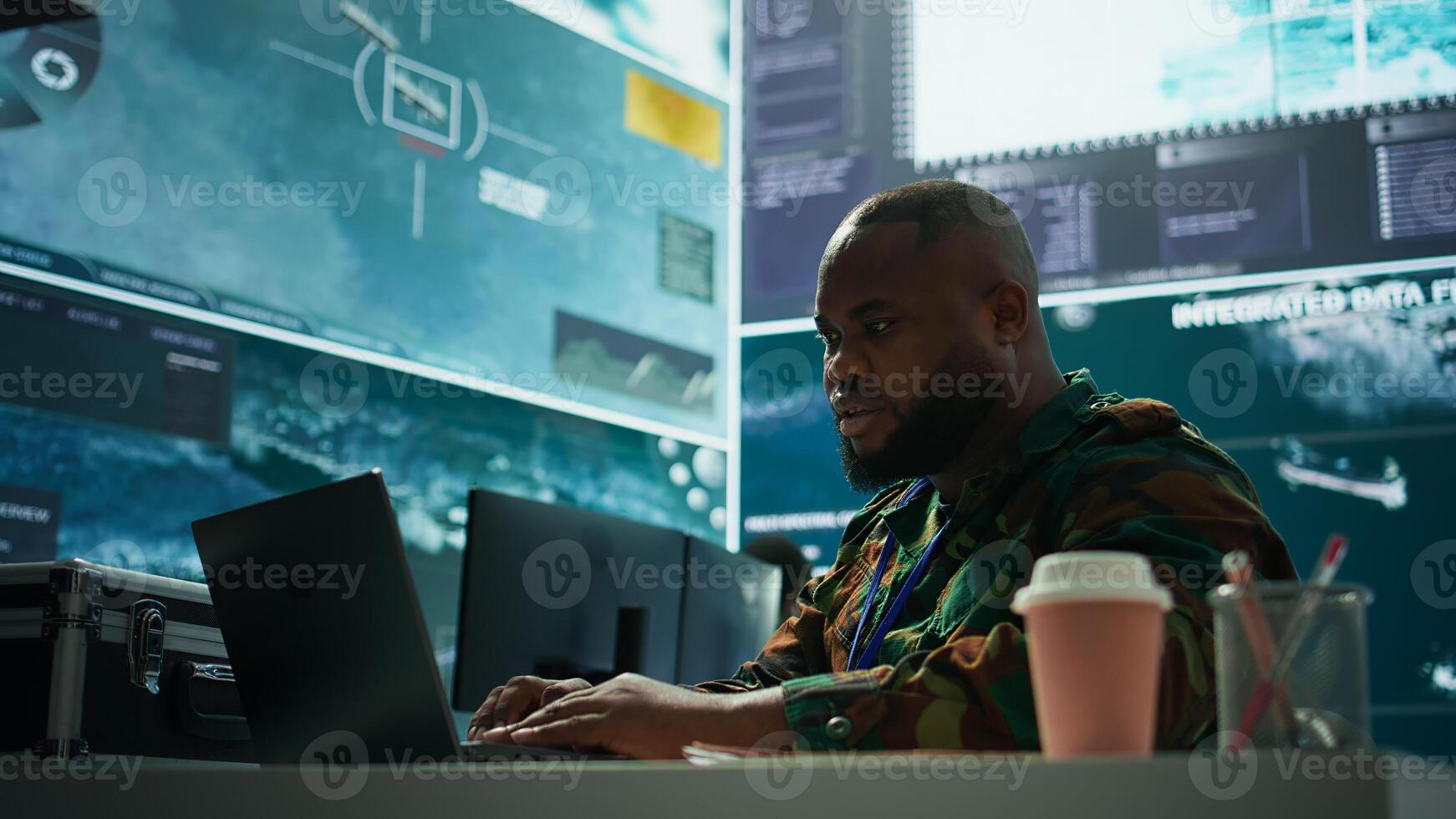 IT analyst in a high tech base of operations handling surveillance activity and ensuring security protocols. Military command post crew collecting real time data to achieve objectives. Camera B. photo