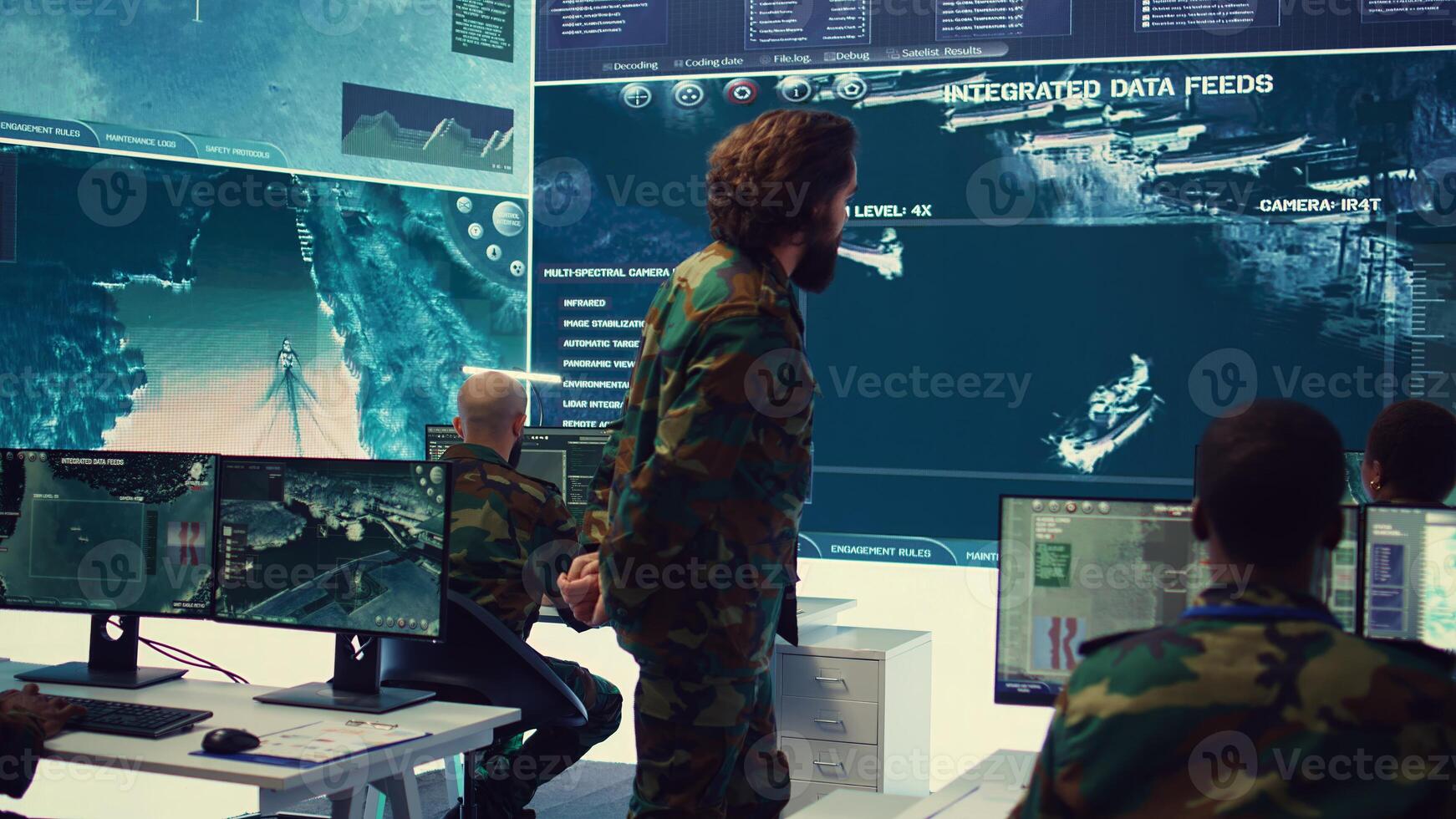 Staff sergeant briefing his army troops crew with details of a new mission, operating command center devices to monitor radar CCTV footage and provide information to people in the field. Camera B. photo