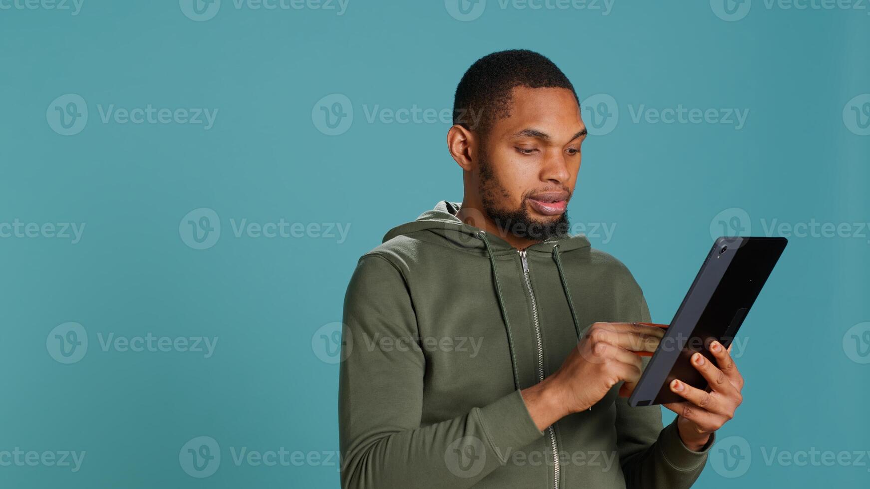 Upbeat man adding payment method on online website using tablet. Person thrilled to do internet shopping using device, typing debit card data, isolated over studio background, camera A photo