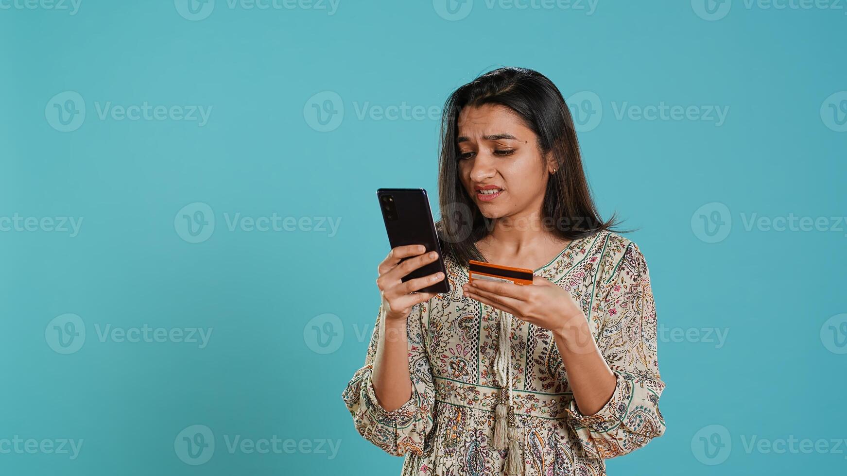 Woman adding payment method on shopping website using phone, taking advantage of promotions, studio background. Indian person buying stuff online using credit card, typing data on device, camera A photo