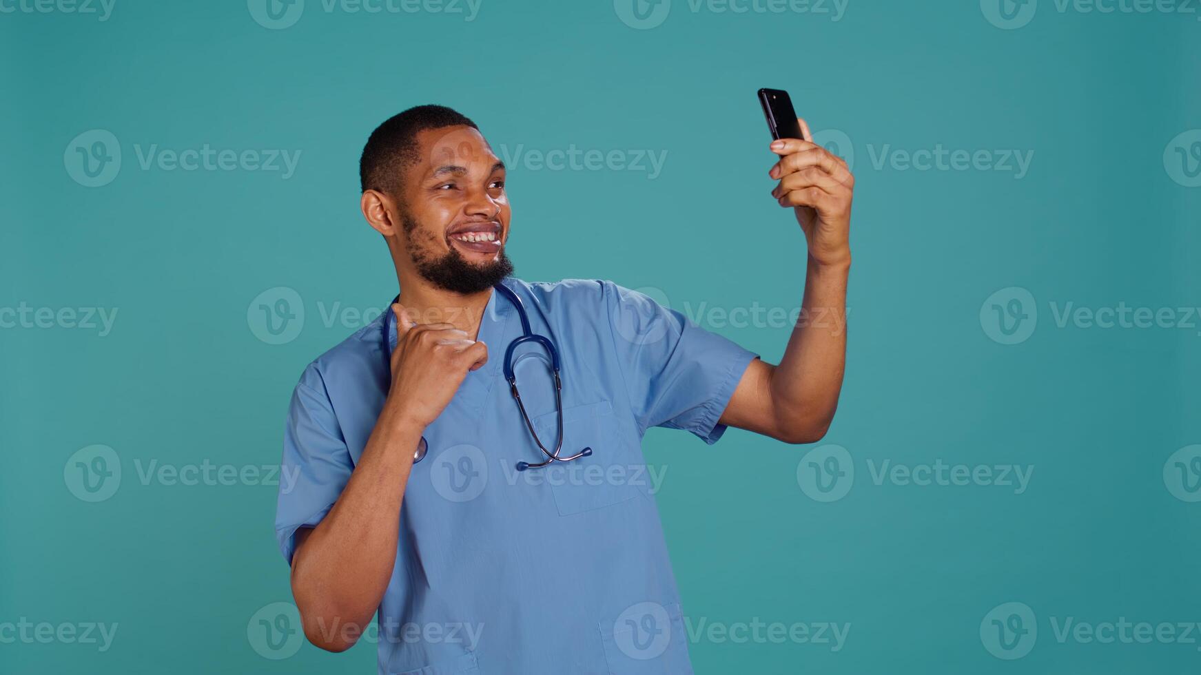 Male nurse using mobile phone to take selfies during hospital job shift break. Healthcare worker using smartphone to take pictures of himself, isolated over studio background, camera B photo